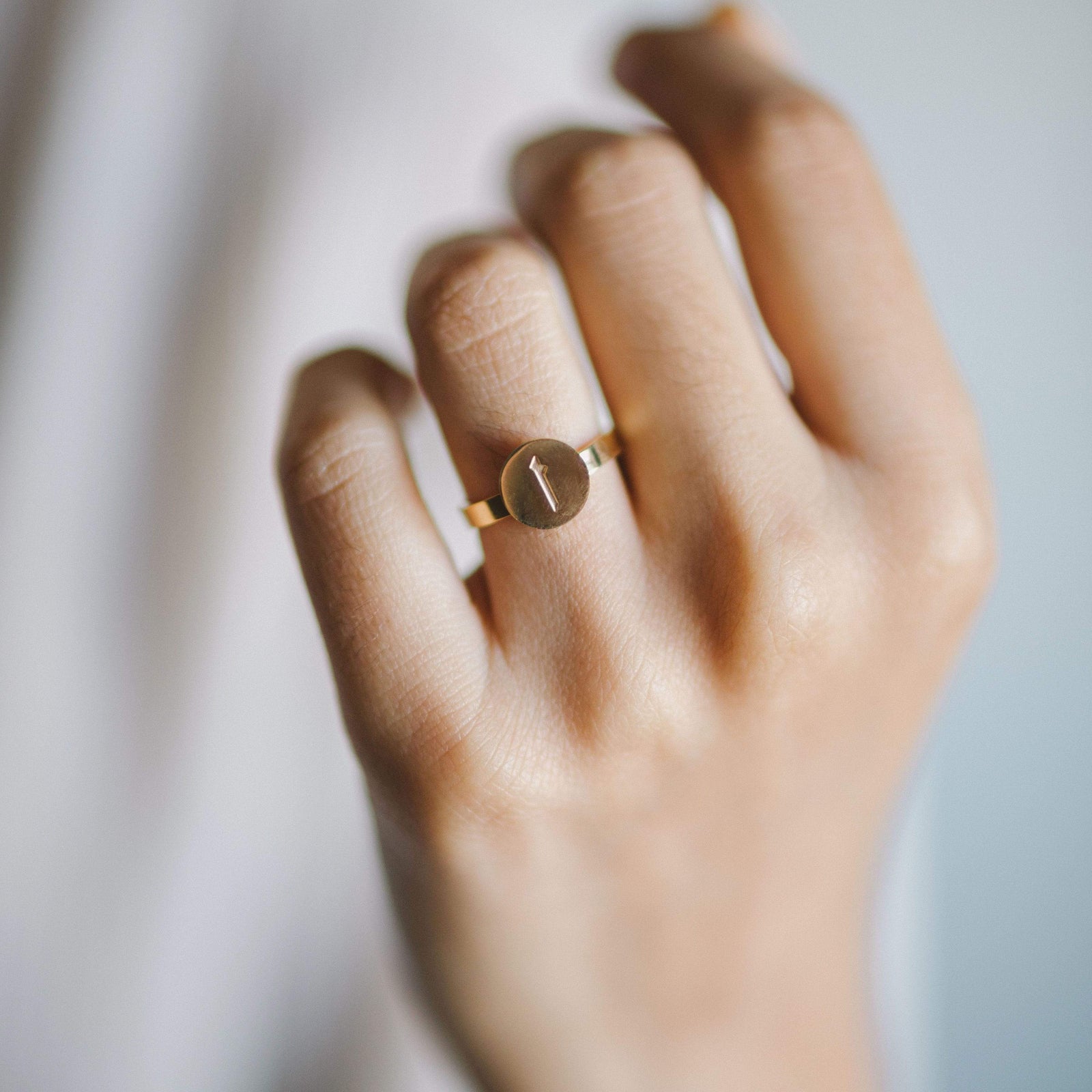 Hand wearing a gold ring with a circular face engraved with an Arabic letter.
