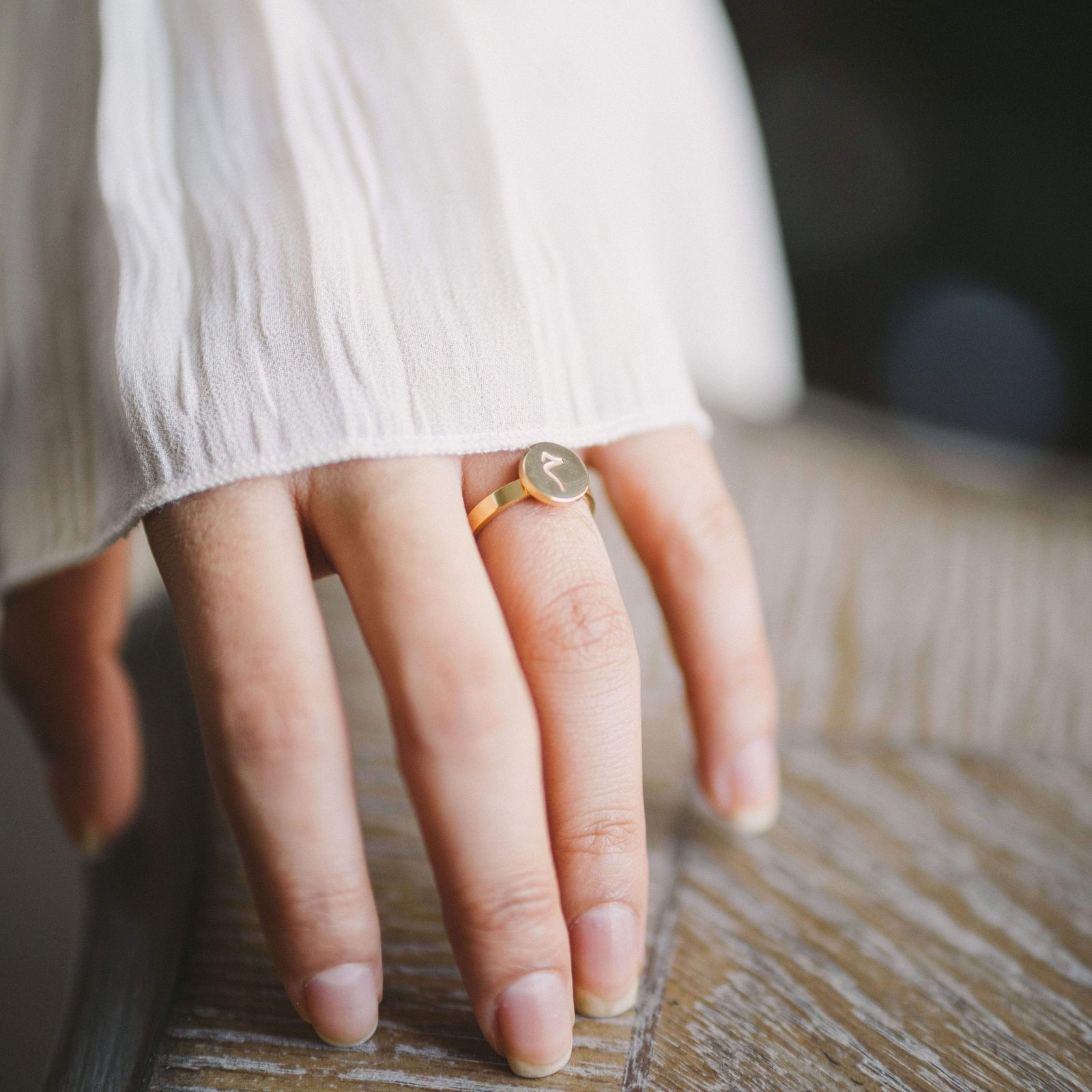 Hand wearing a gold ring with a circular face engraved with an Arabic letter.
