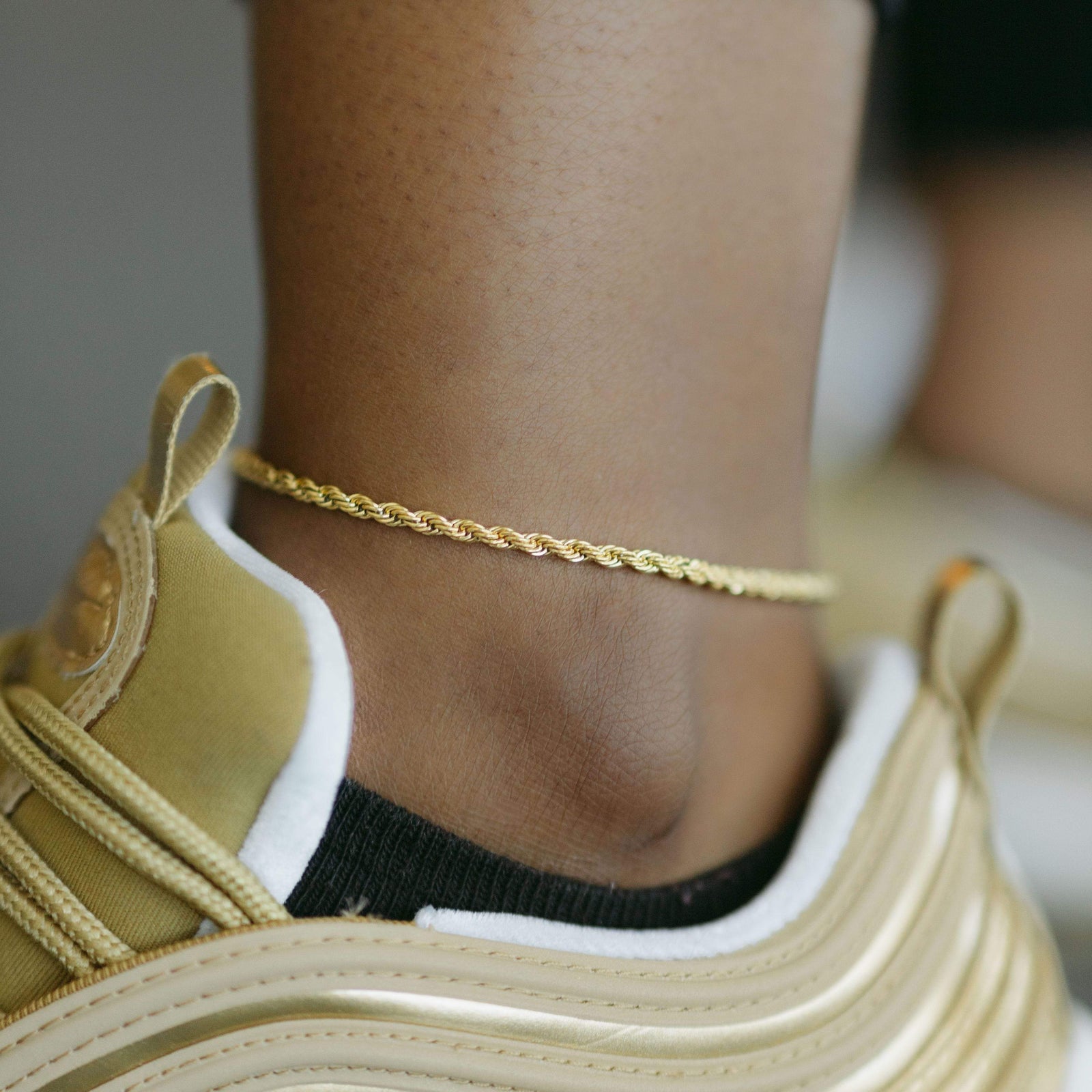 Gold rope chain anklet worn above a gold and white sneaker.