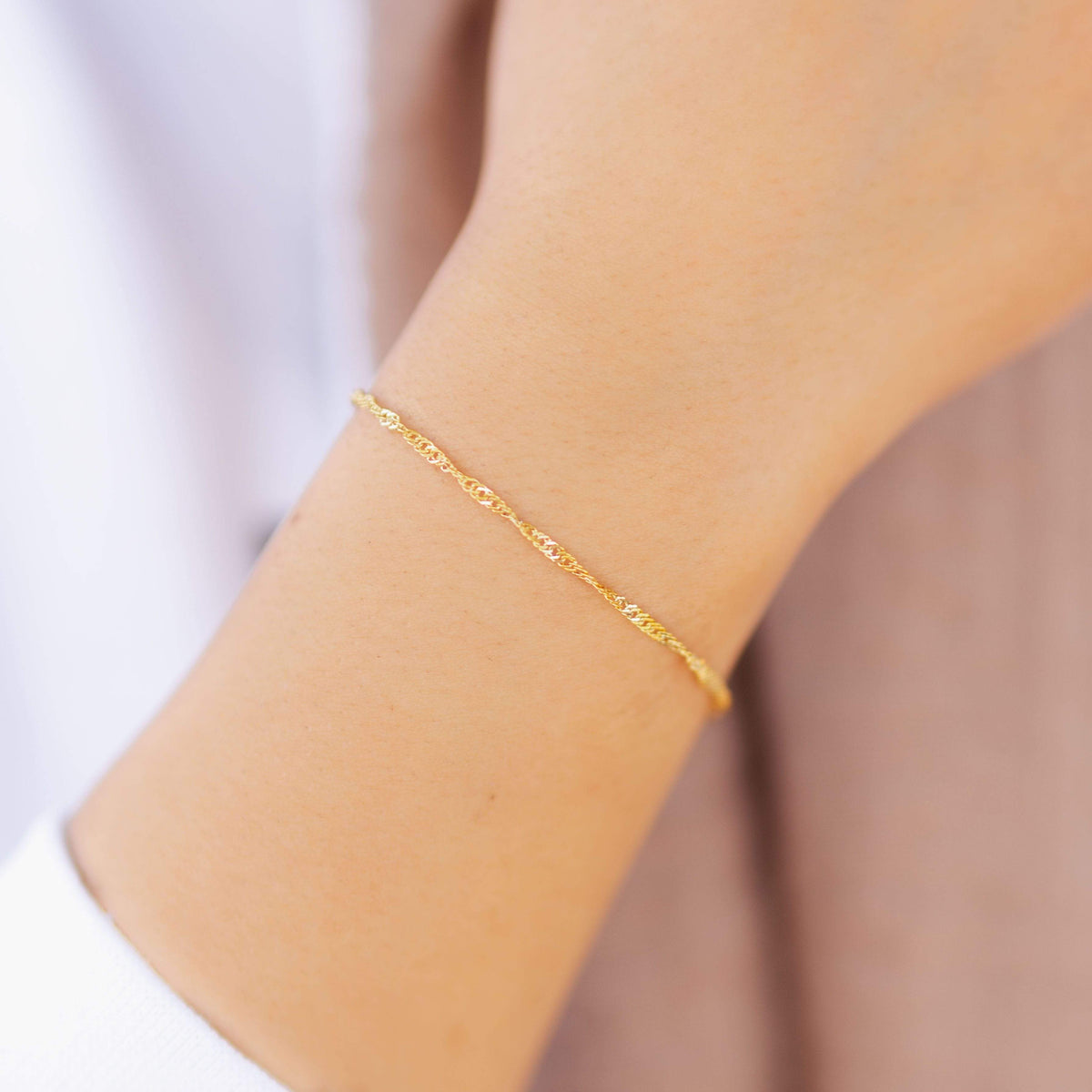 Woman wearing the thinnest gold twisted chain bracelet on her wrist, styled with a light outfit. 