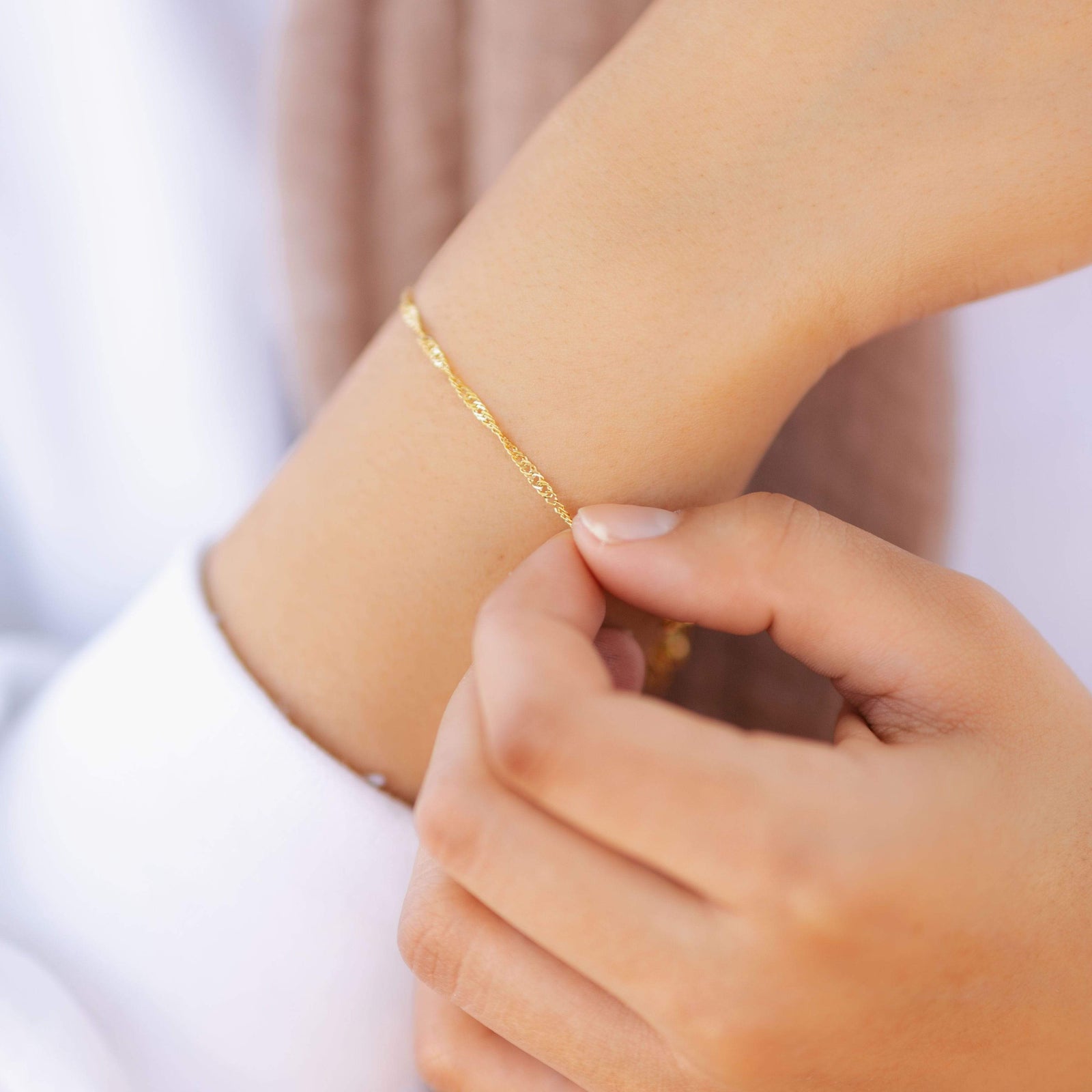 Close-up of a woman’s hand adjusting the thin gold twisted bracelet on her wrist.