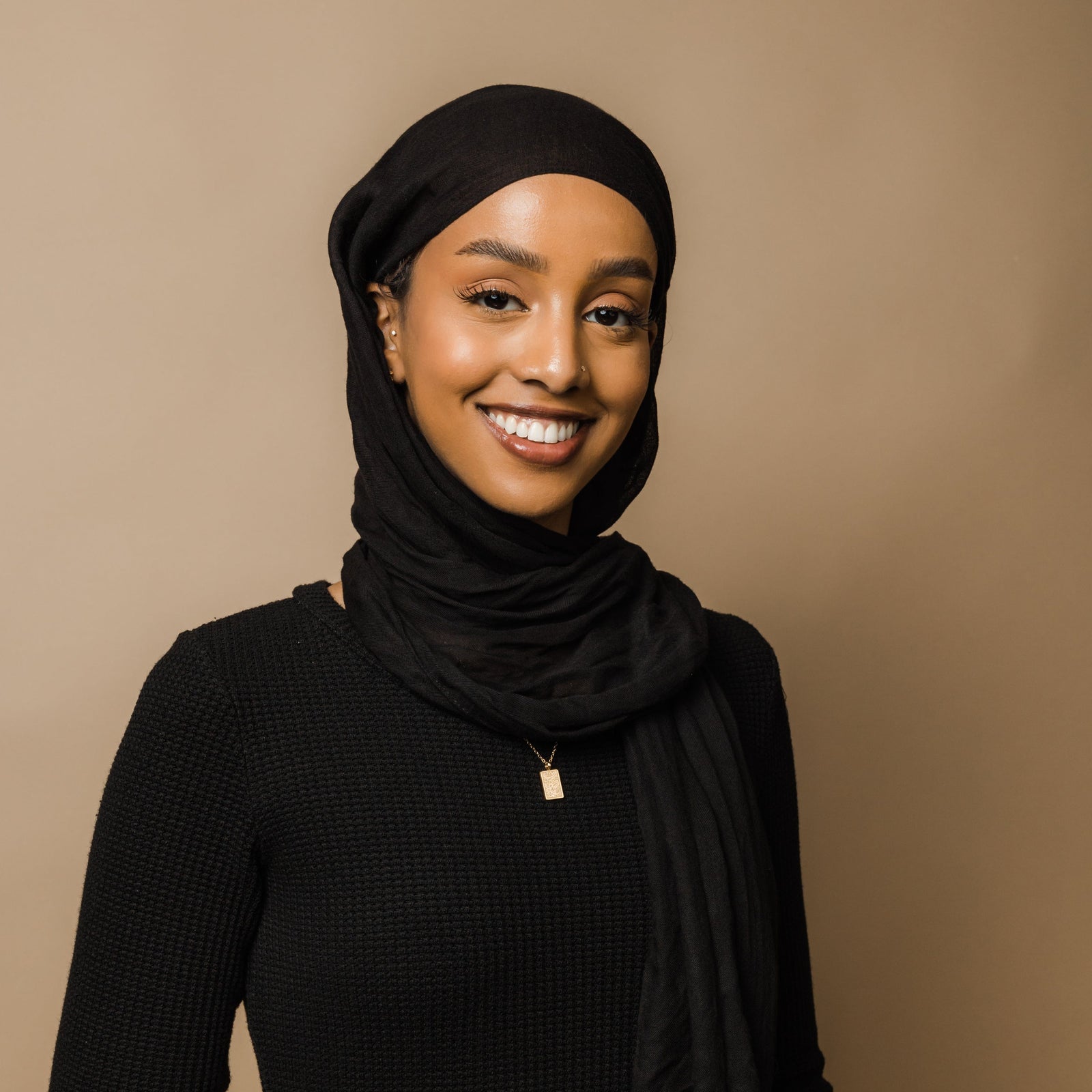 Photo of the model smiling to the camera wearing the gold Knowledge Necklace.