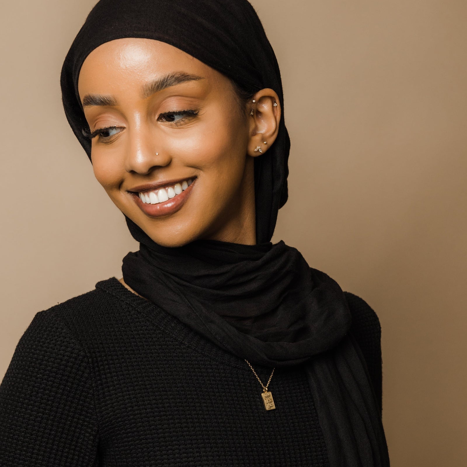 Photo of the model looking away to the camera, smiling. The model is wearing the gold Knowledge Necklace.