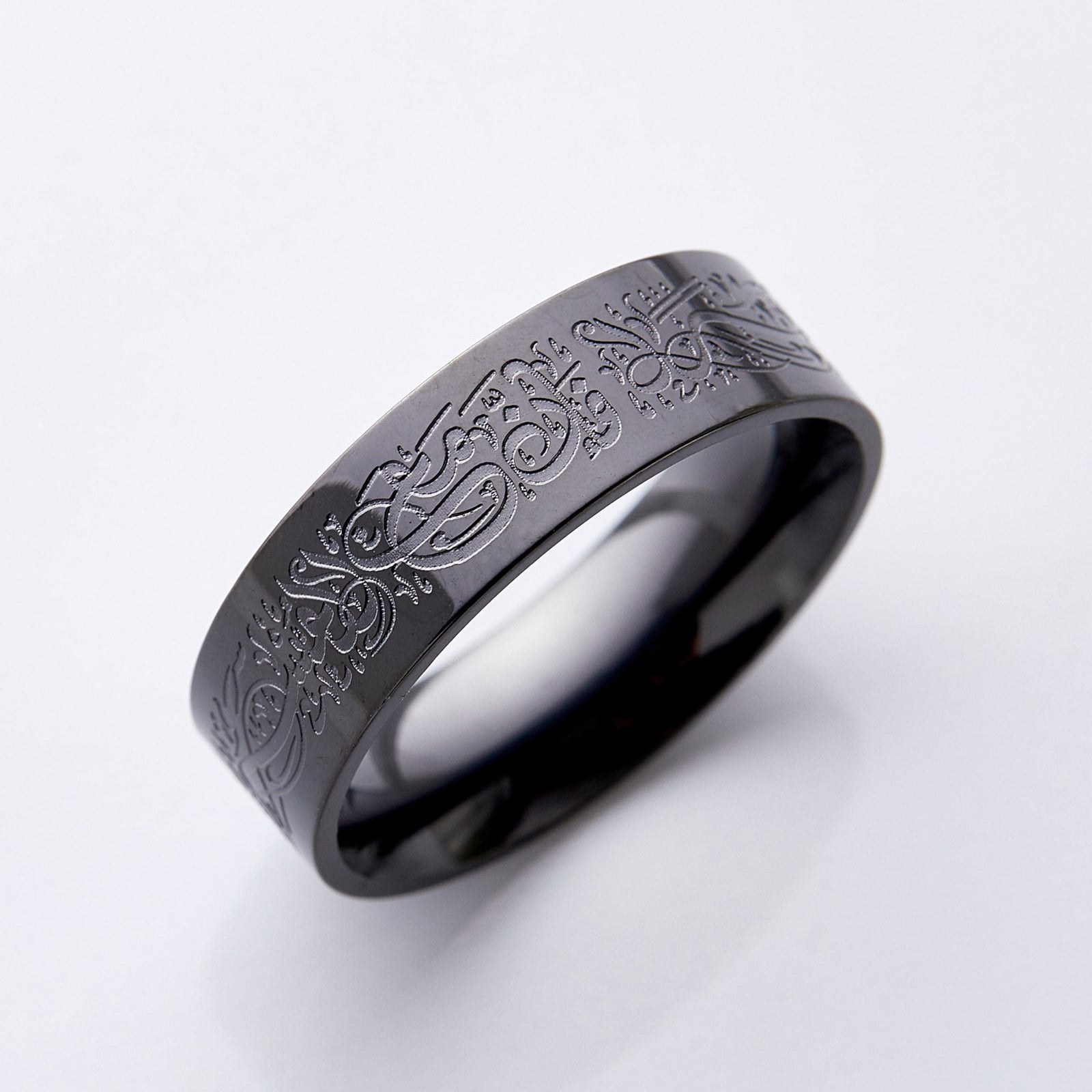 Photo of a black band ring that is designed with an Arabic Calligraphy that engraving that means "Verily, with hardship comes ease. With hardship comes ease."