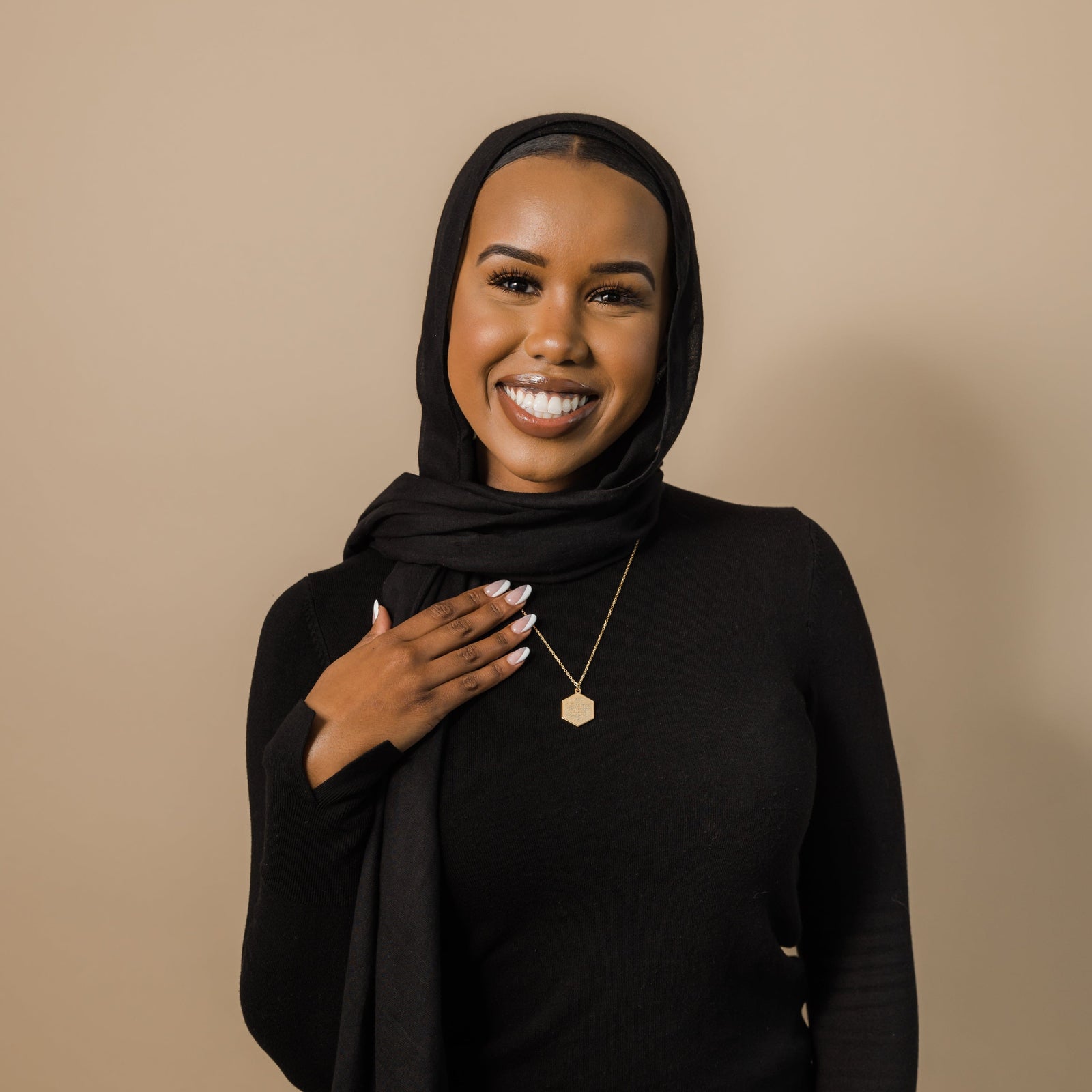 Photo of the model smiling to the camera. The model is wearing the gold Surat Al-Fatiha Necklace.