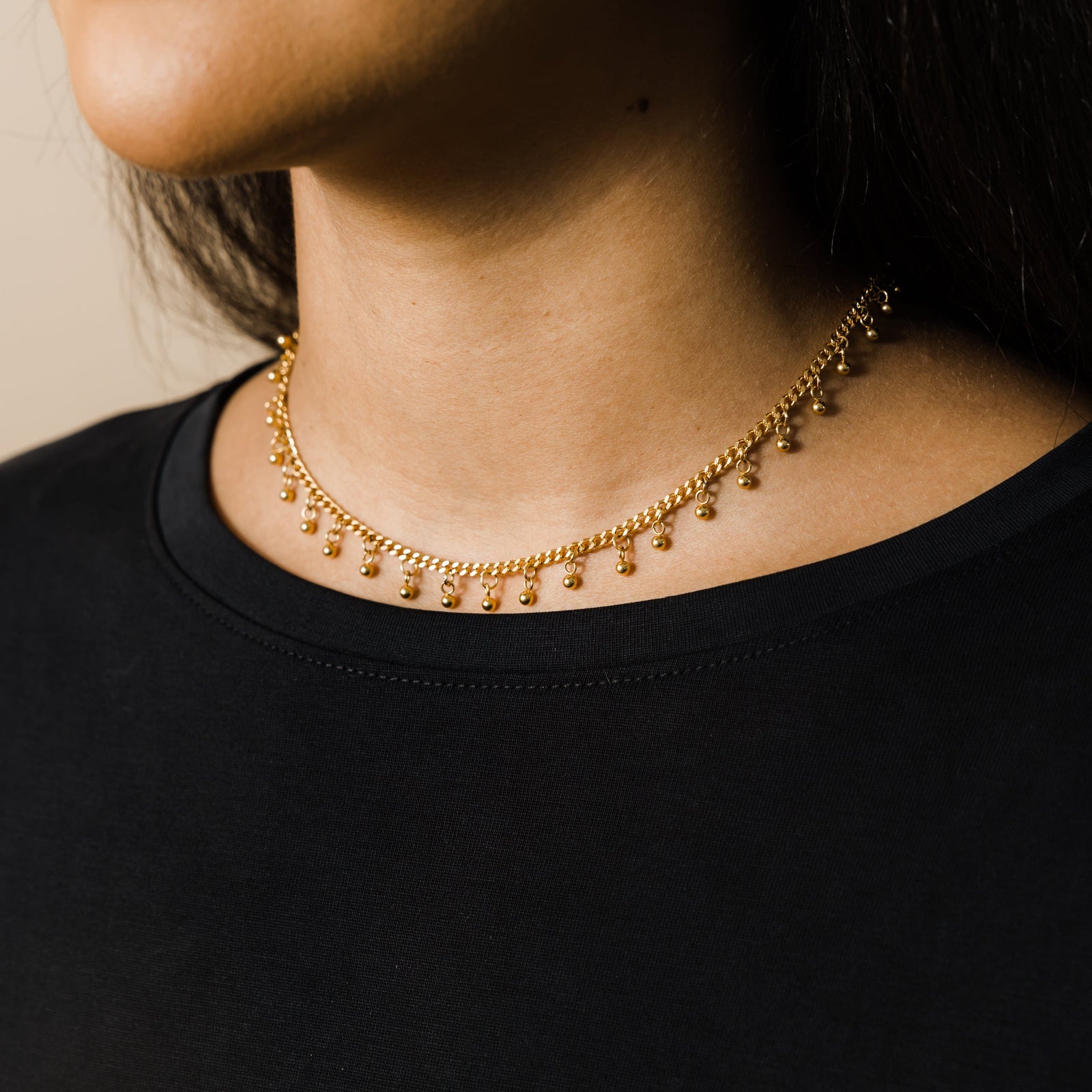 Close-up of a gold choker with dangling bead accents worn by a woman in a black top.