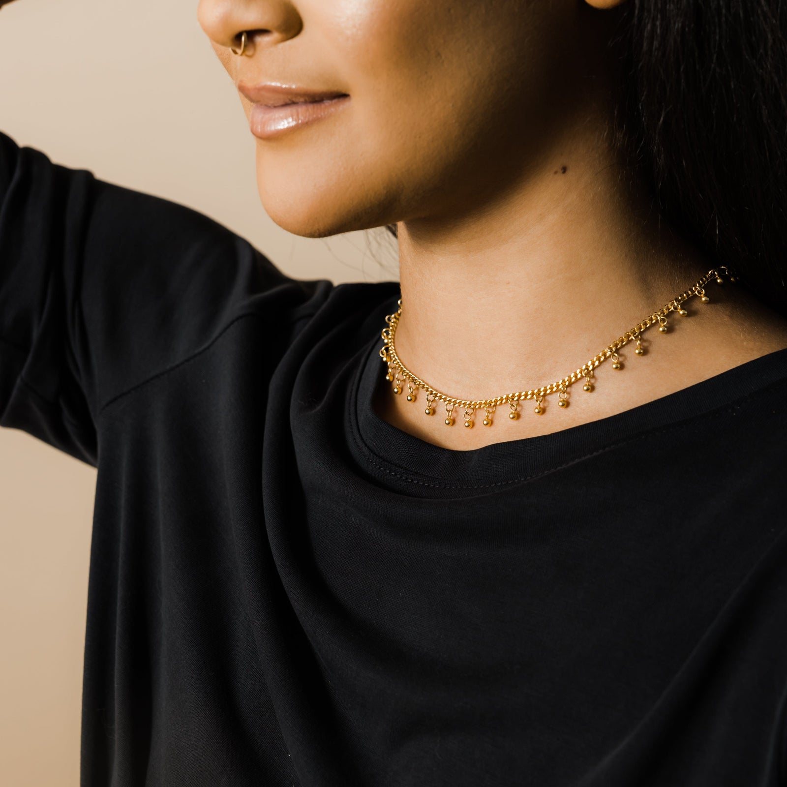 Woman smiling, wearing a gold choker with dangling beads, dressed in a black top.