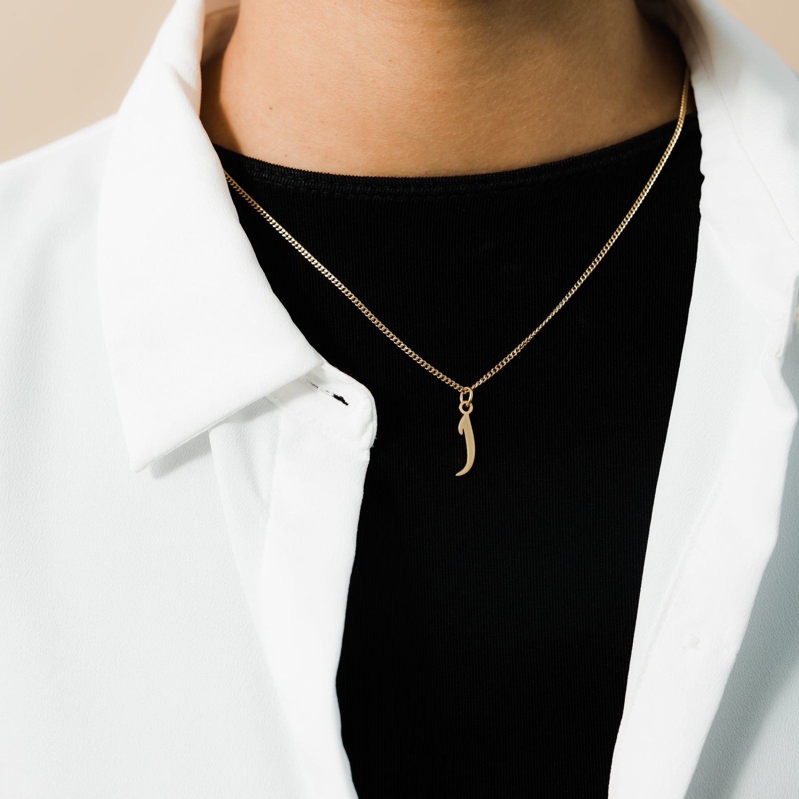 The gold Hanging Arabic Letter Necklace as worn by the model.