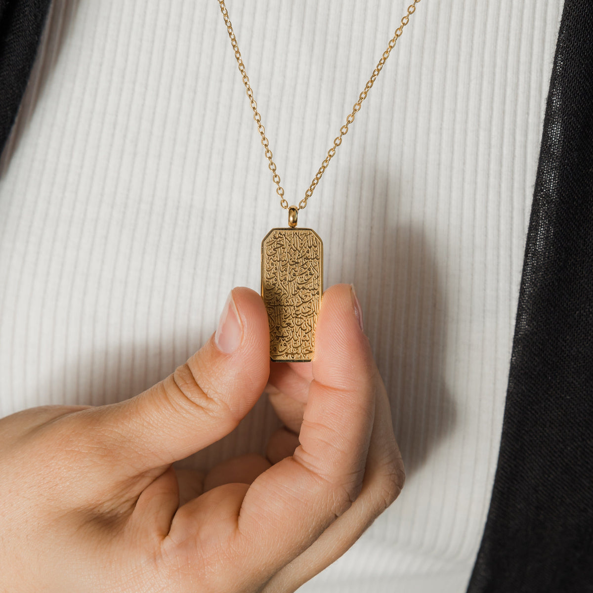 Photo of the model holding the gold plated tag of the necklace they are wearing.