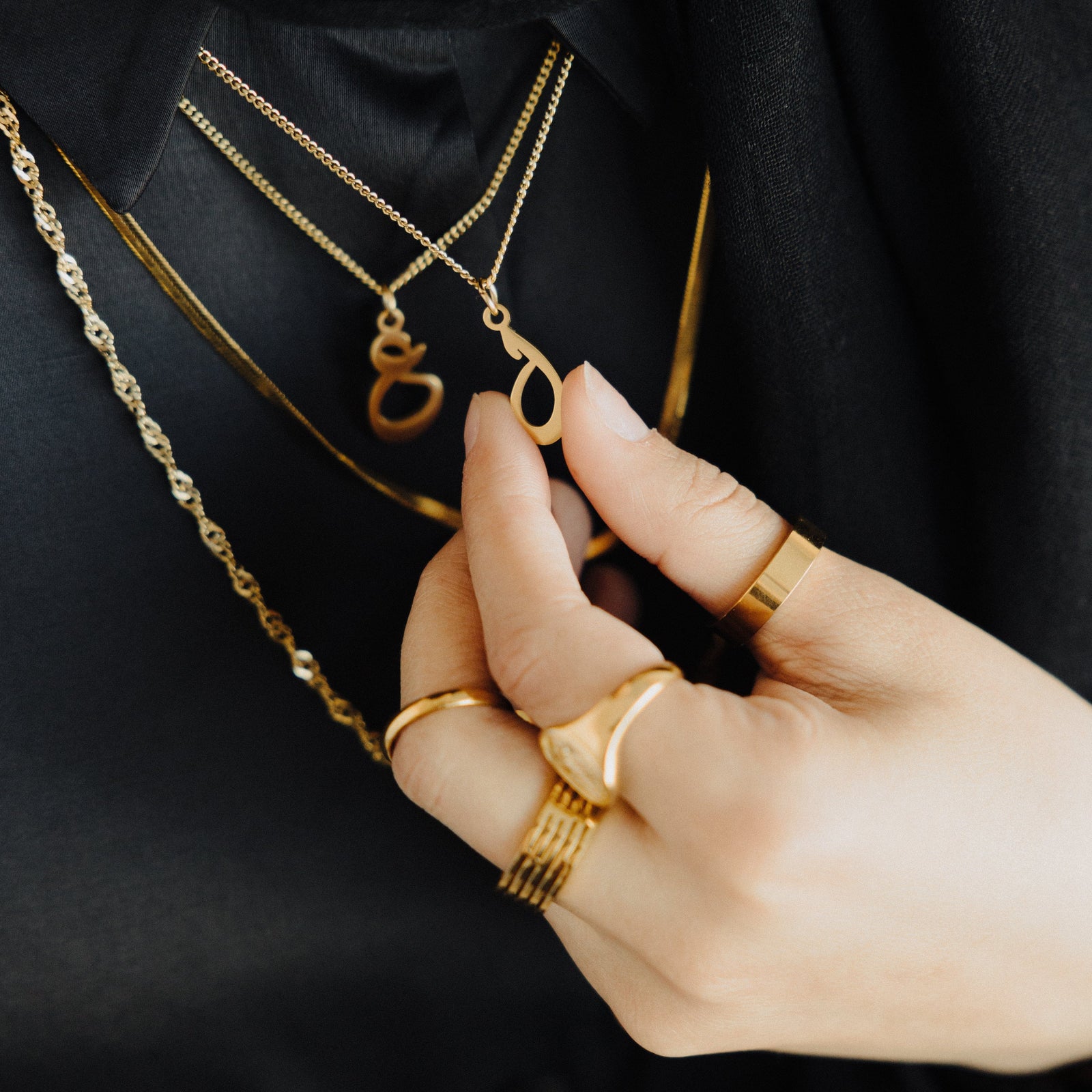 Close up of the gold Hanging Arabic Letter Necklace as worn by the model
