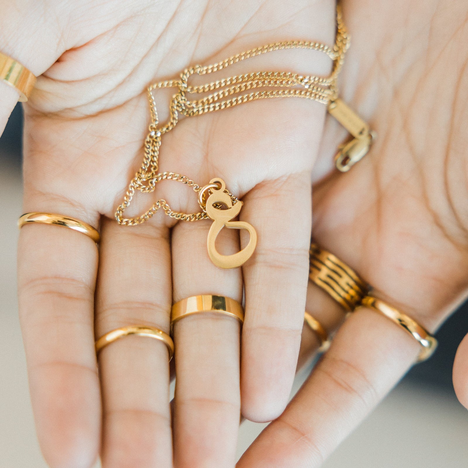 Close up of the gold Hanging Arabic Letter Necklace resting on the model's palm.