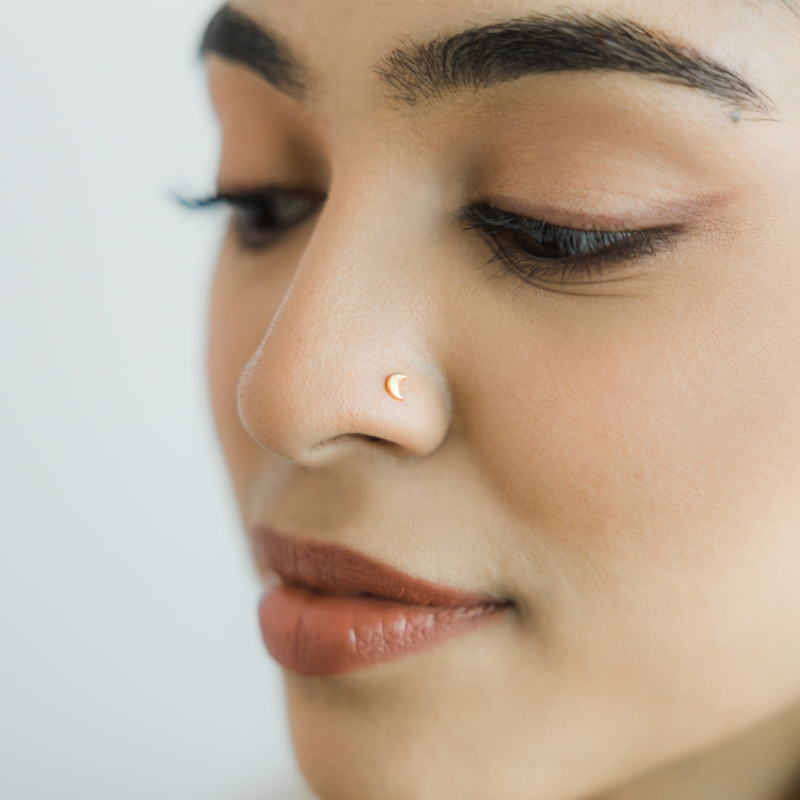 Close up of the model's face to show the gold Crescent Stud Nose Ring they are wearing.