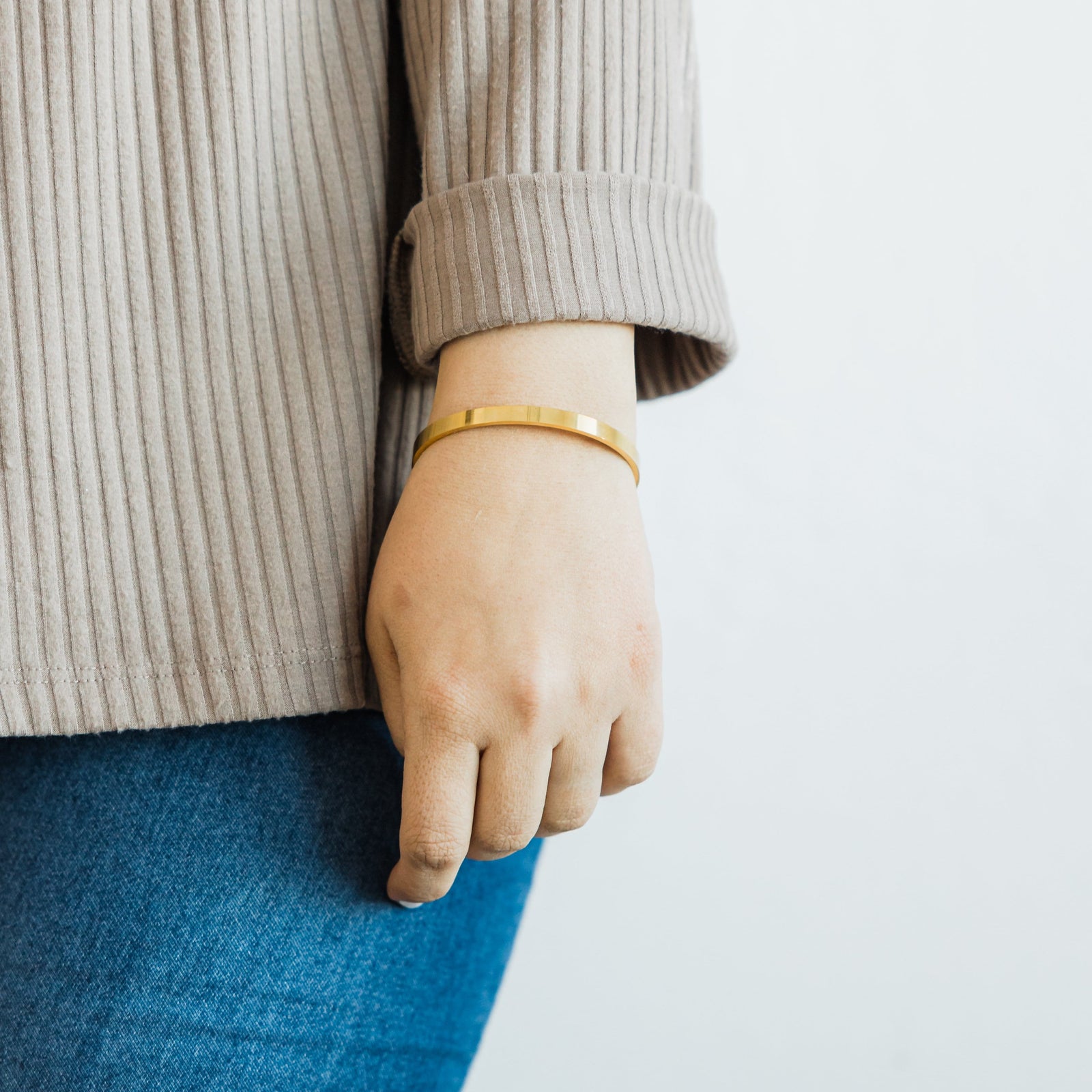 Photo of the gold Essential Bangle as worn by the model on their left wrist.