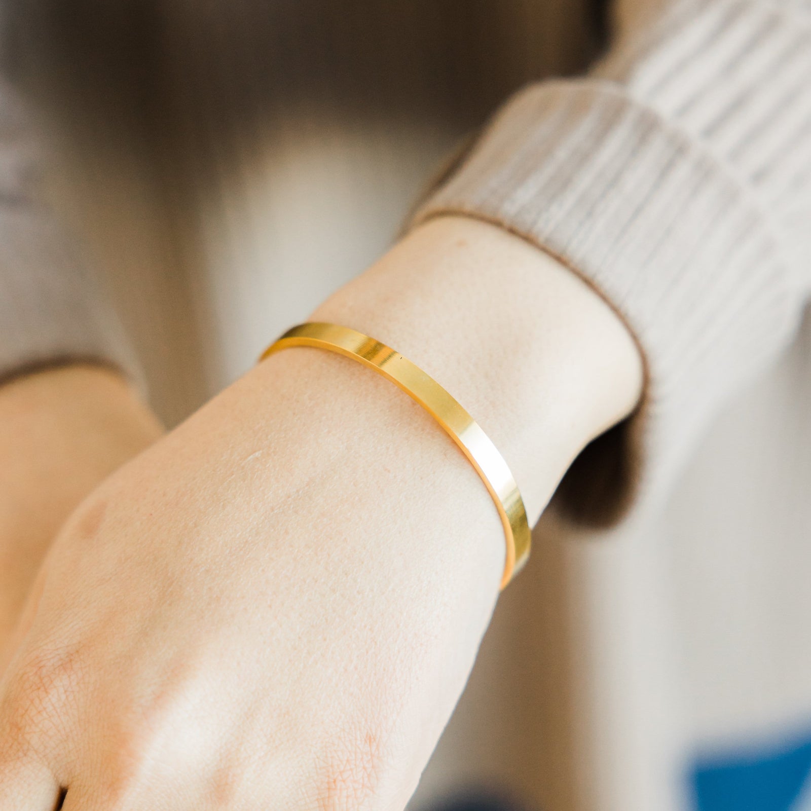 Close up of the gold Essential Bangle as worn by the model on their left wrist