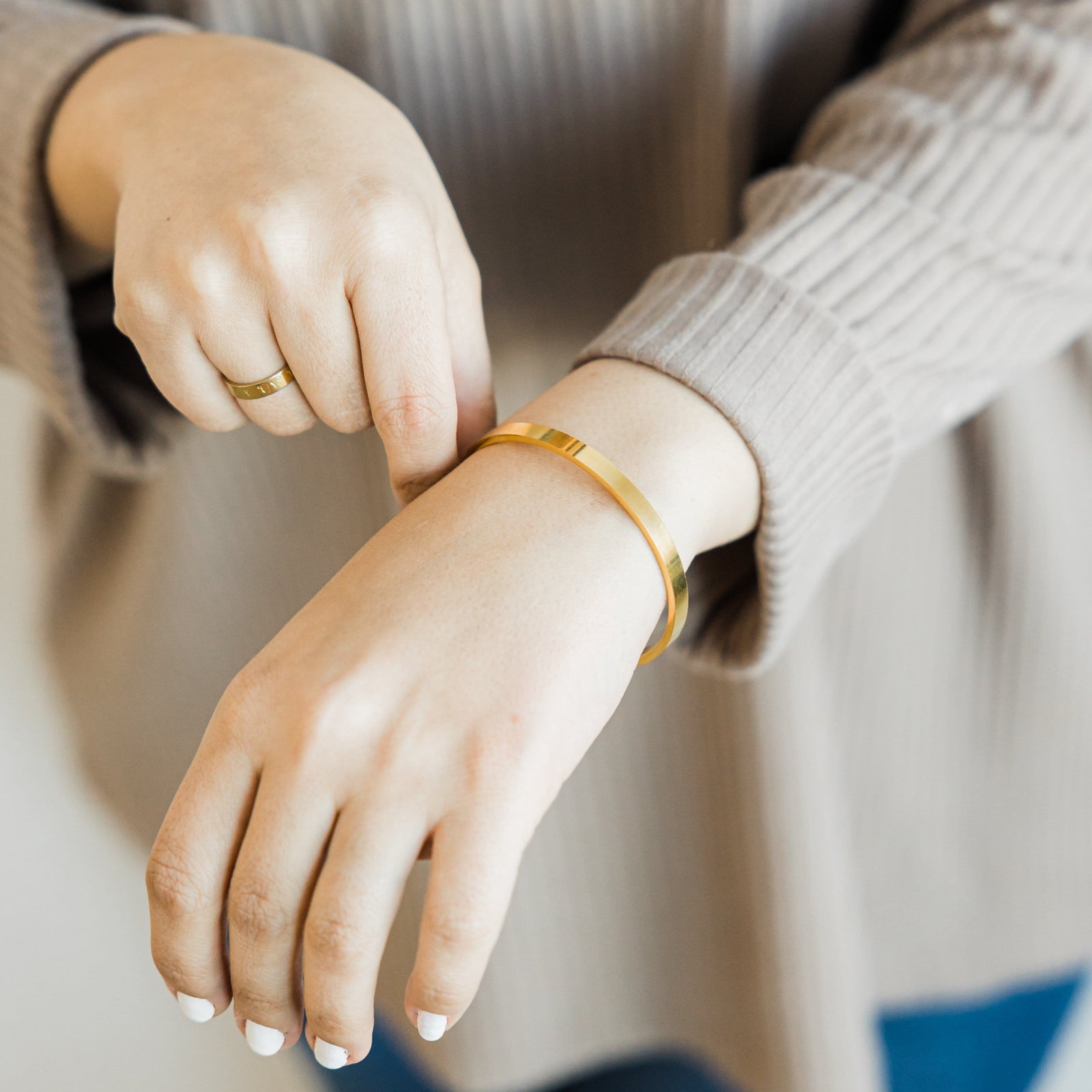 Photo of the models hands. The model is wearing the gold Essential Bangle on their left wrist.