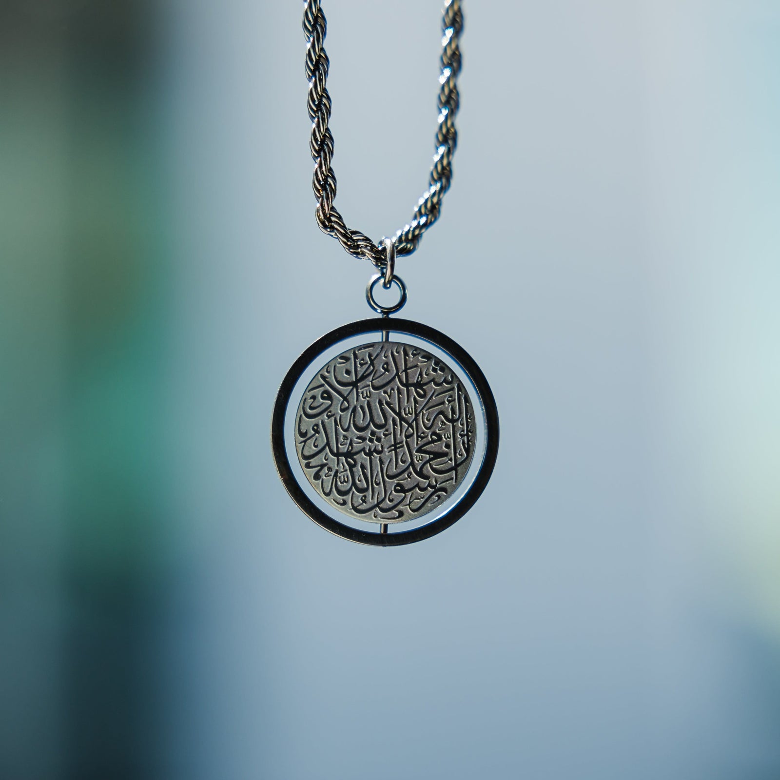 Black car hanger with a circular Shahada pendant, suspended and photographed in focus against a blurred background.