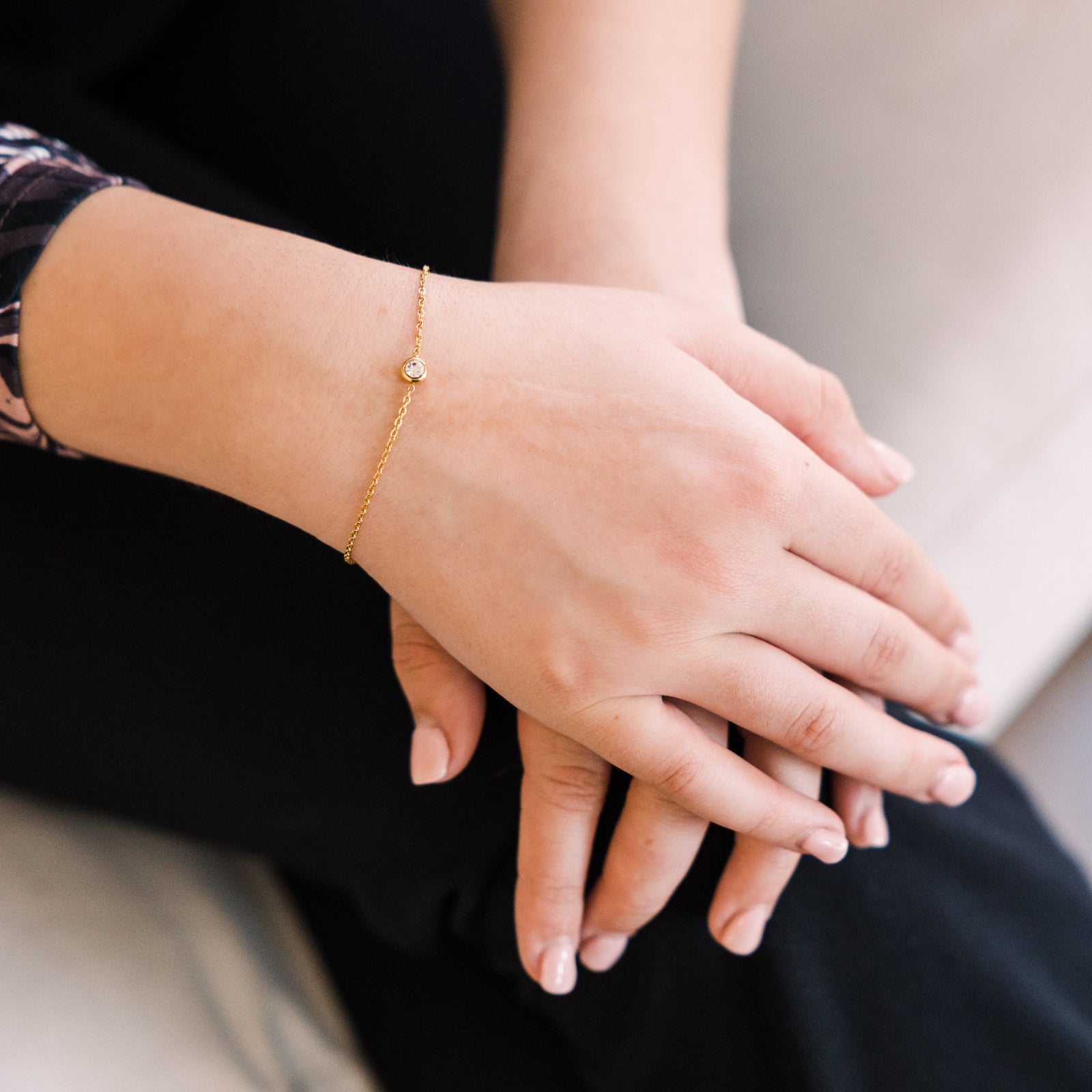 Photo of the model's hand over the other. The model is wearing the gold Bezel Bracelet on their right wrist.