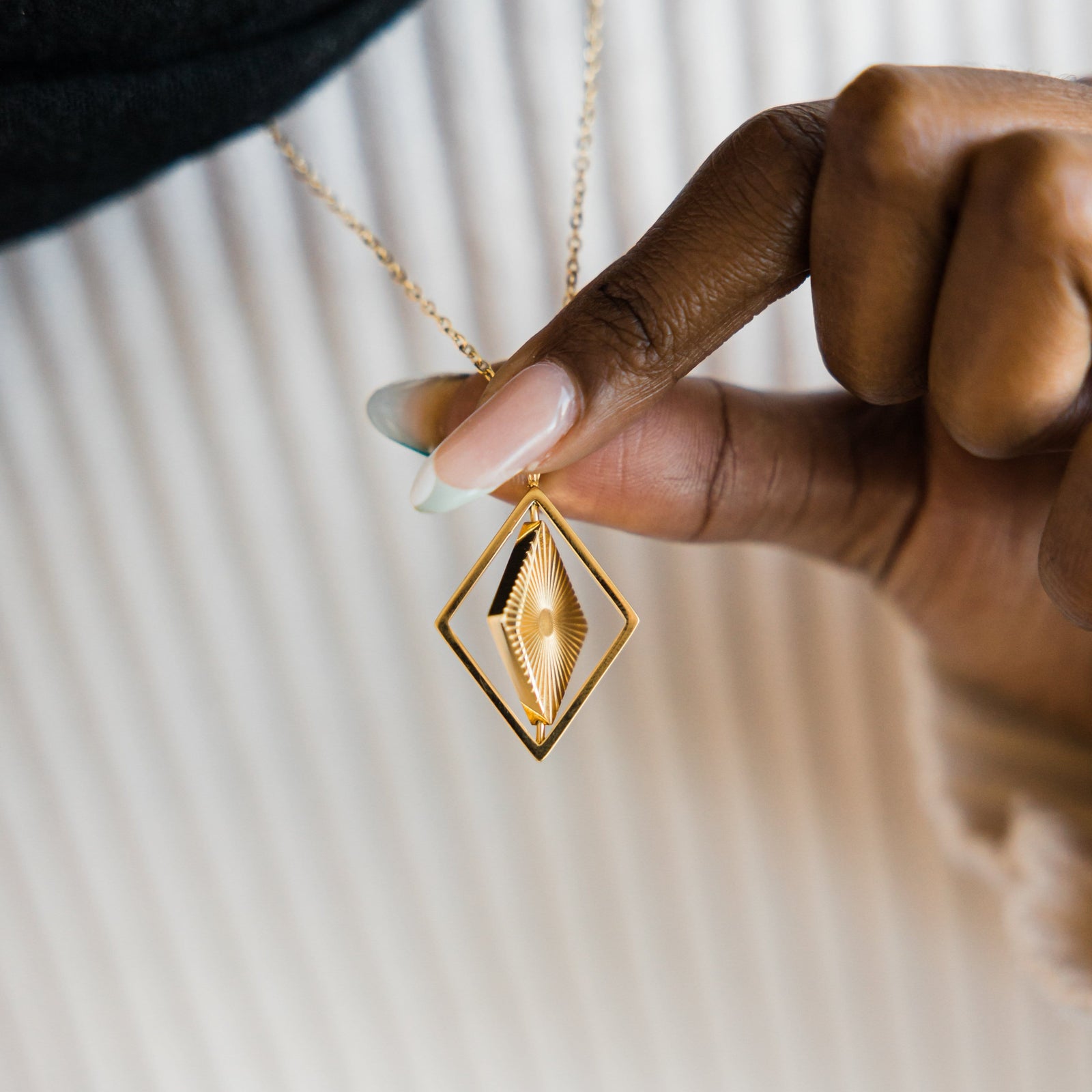 Close up of the gold Sun Rays Necklace as the model holds the pendant to show its design.