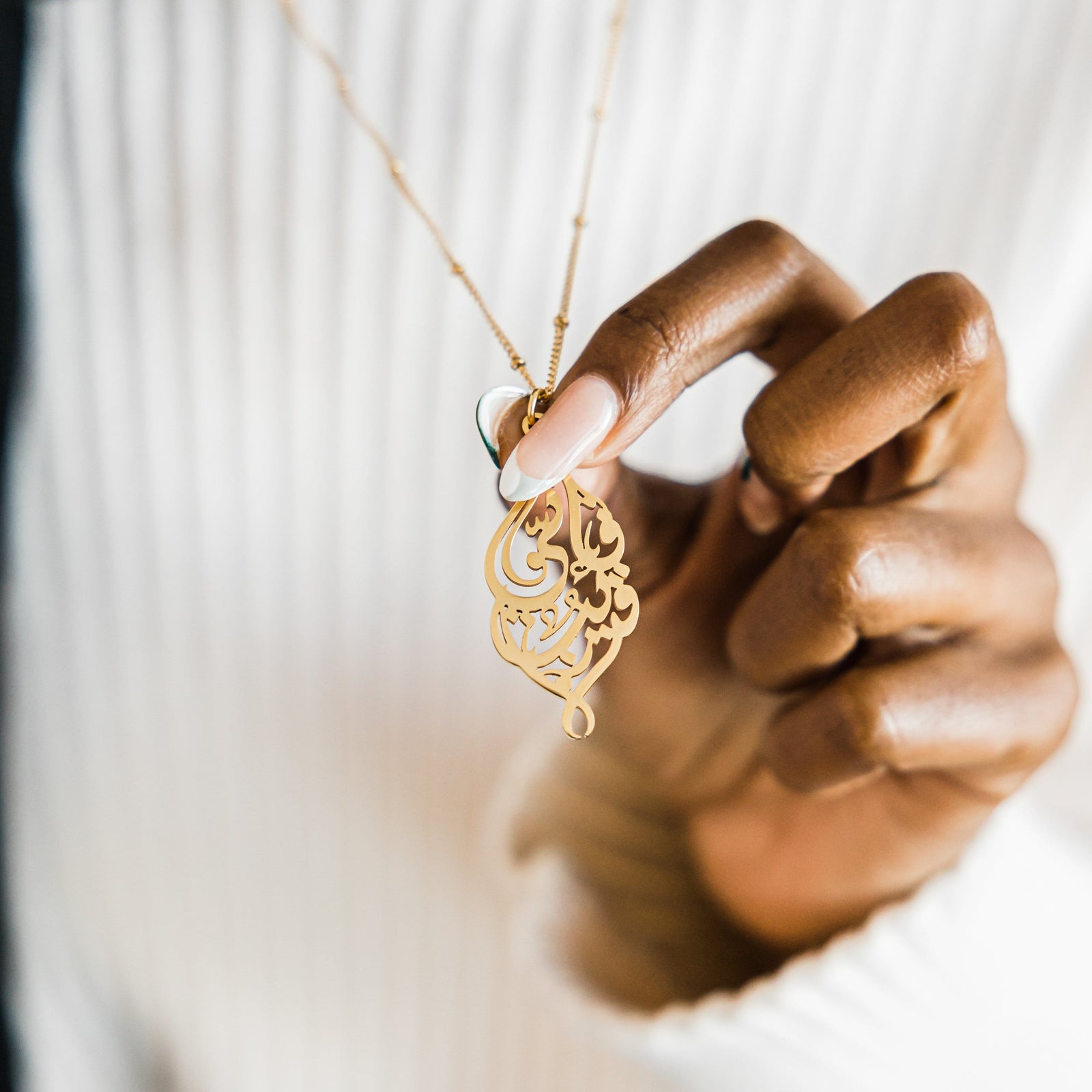 Close up of the gold "I Am Near" necklace as the model holds the pendant closer to the camera.