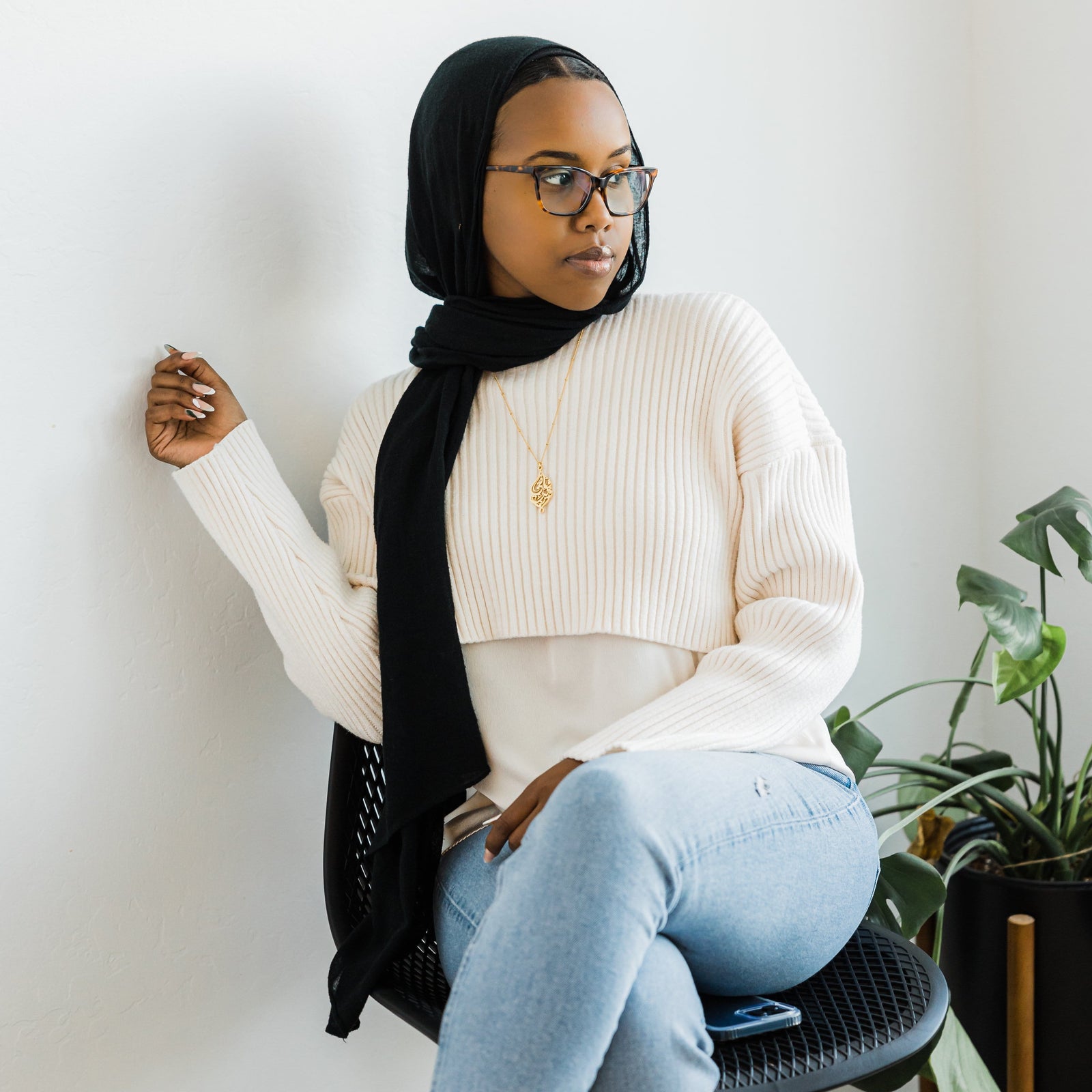Photo of the model sitting on a chair, the mode is wearing the gold "I Am Near" necklace.