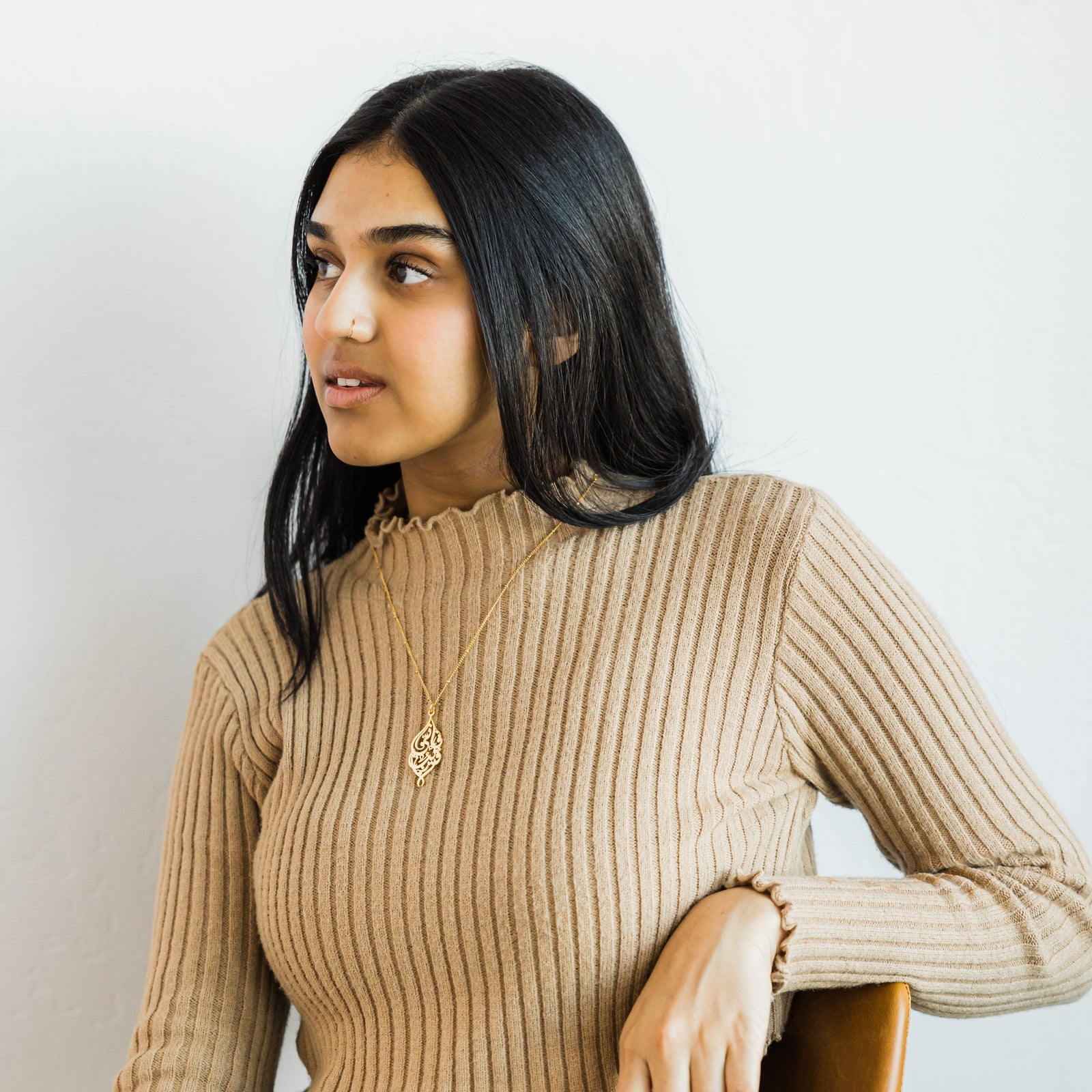 Photo of a model styled in a beige long sleeves shirt. The model is wearing the gold "I Am Near" Necklace.