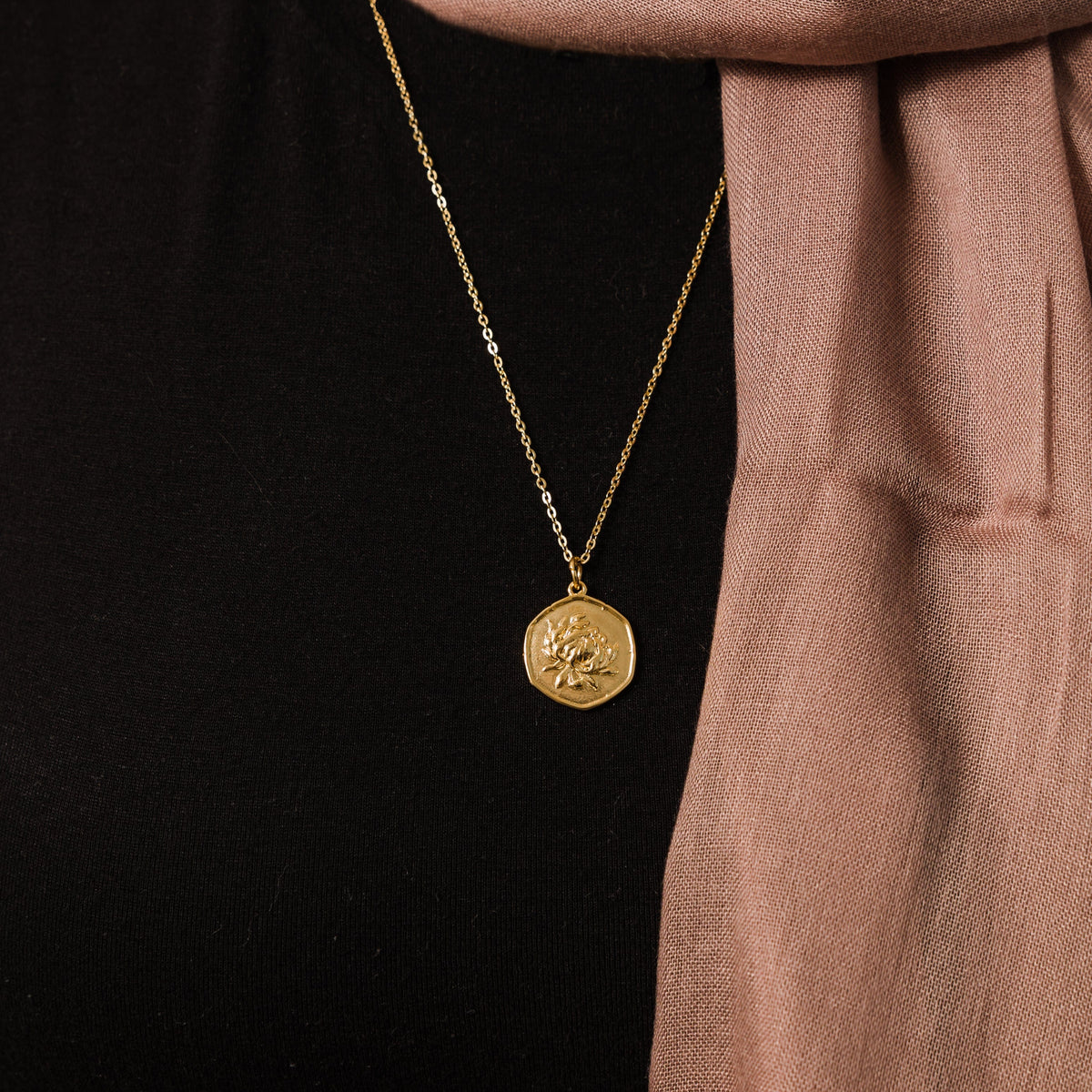 Close up of the gold November | Birth Flower Pendant against the black fabric of the model's clothing