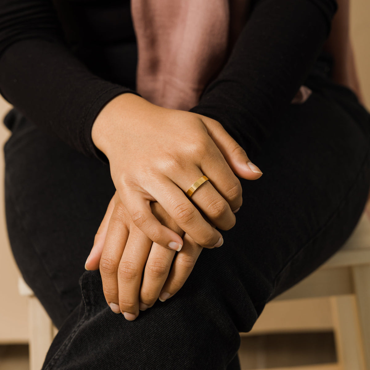 Close-up of a gold band ring worn on the hand of a seated woman dressed in black.