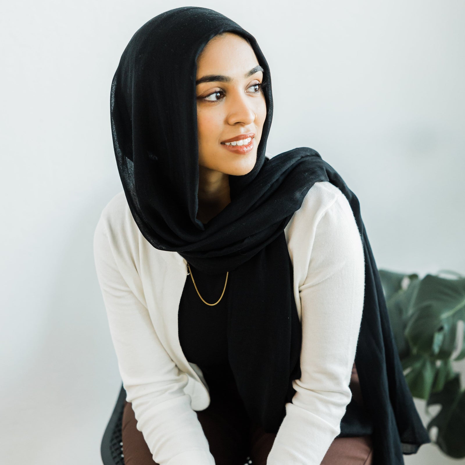 A woman in a black hijab and cream cardigan wearing a single medium-length Cuban chain over a black top.