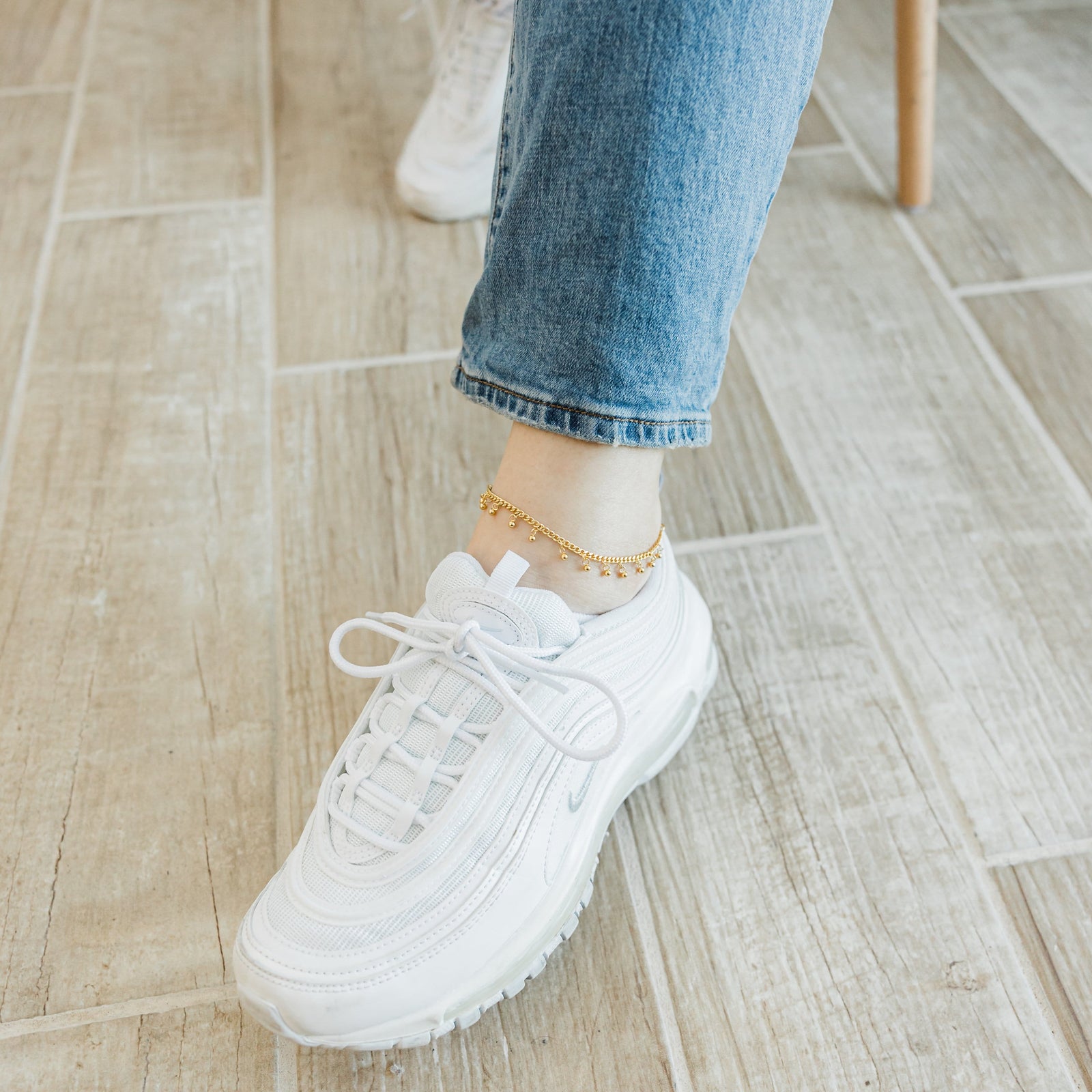 A model wearing the 18K gold-plated Dangling Dotted Anklet. The anklet rests gracefully on her ankle, highlighting the dangling ball-shaped charms against her skin.