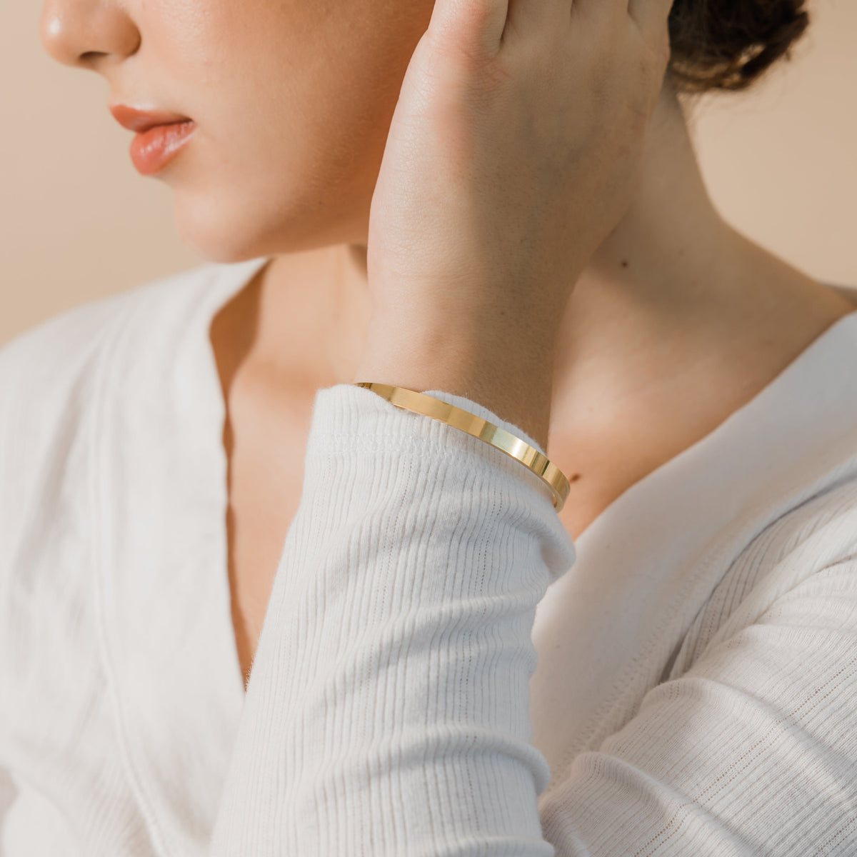 Close up of the gold Essential Bangle as worn by the model on their left wrist.