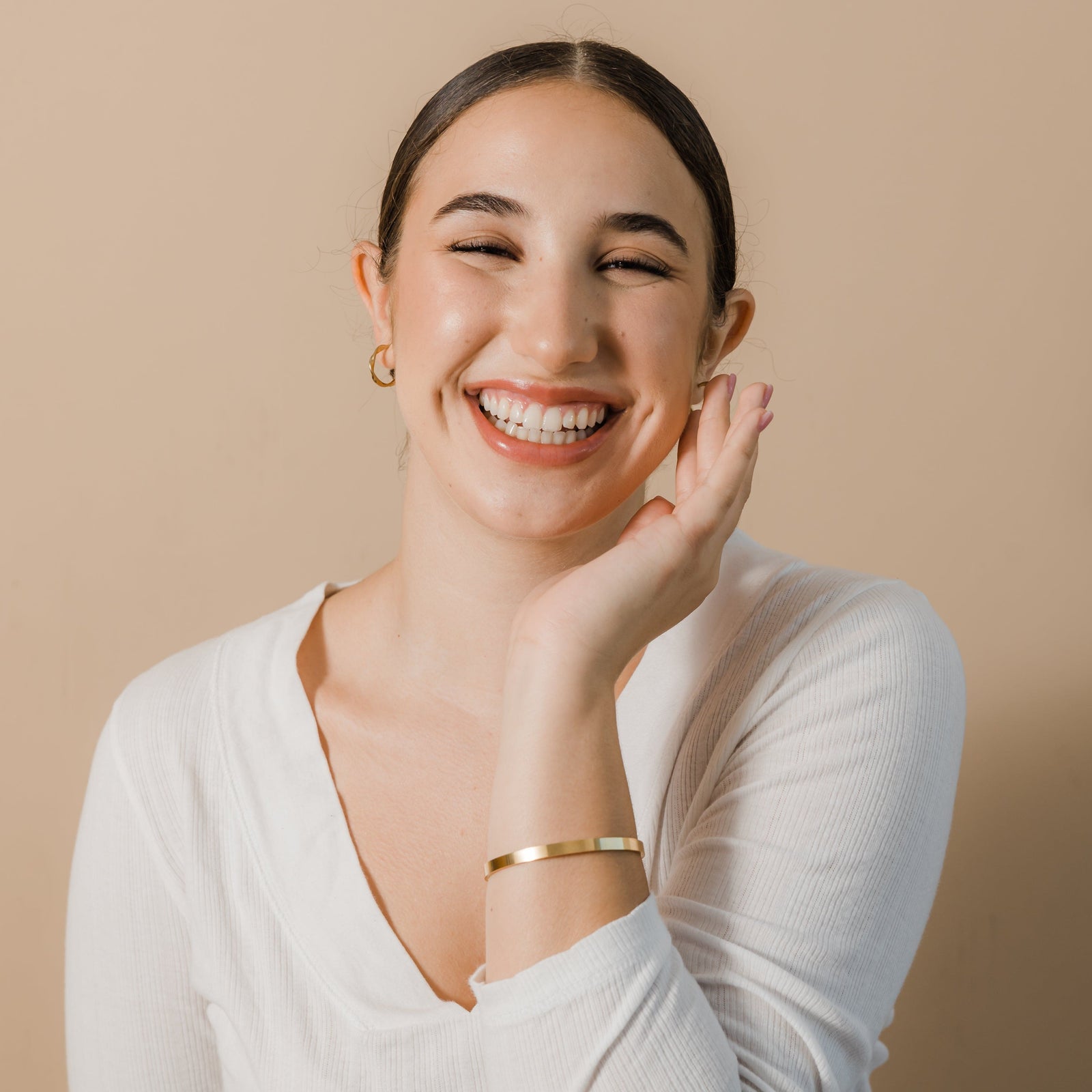 Photo of the model smiling to the camera. The model is wearing the gold Essential Bangle on their left hand.