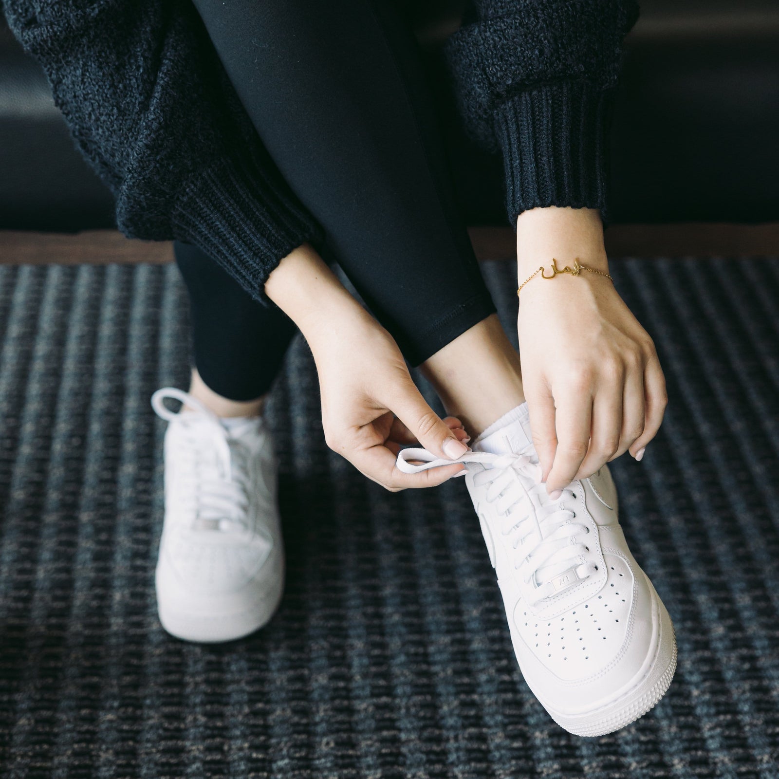 Photo of the model tying their shoelace. The model is wearing the gold Custom Name Bracelet on their left wrist