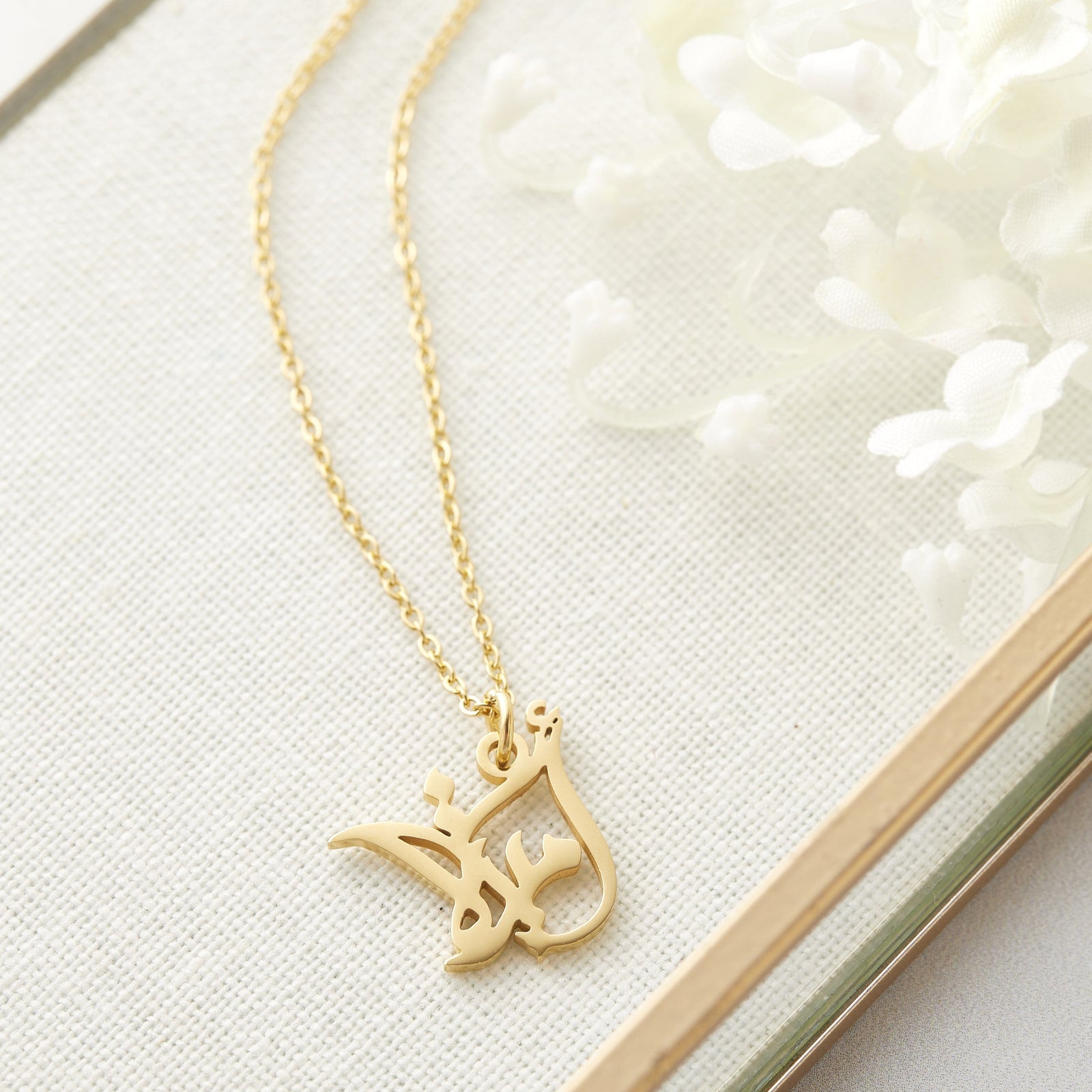 Close up of the gold Ready Calligraphy Name Necklace - Amira on a jewelry frame