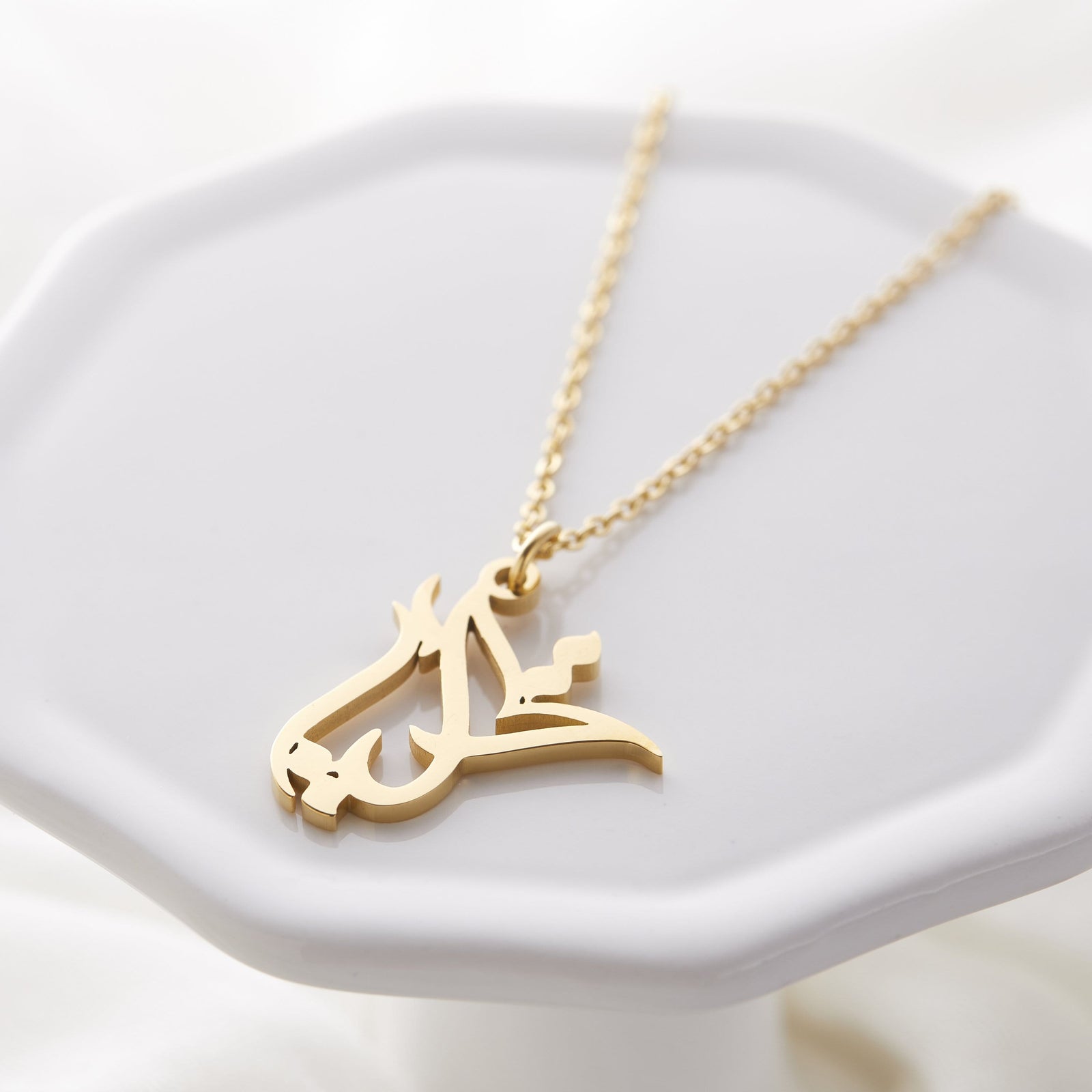 Close up of the gold Ready Calligraphy Name Necklace - Aya against a light background.