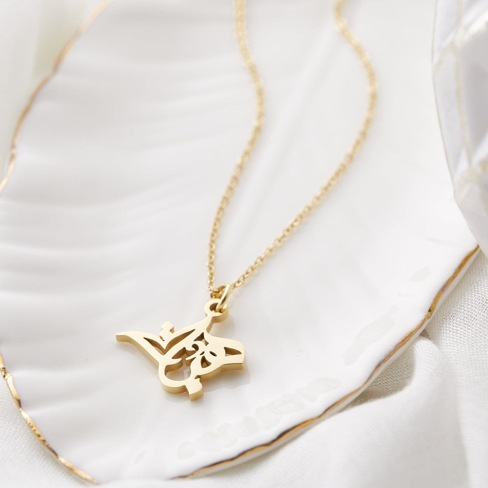 Close up of the gold Ready Calligraphy Name Necklace - Heba against a light background.