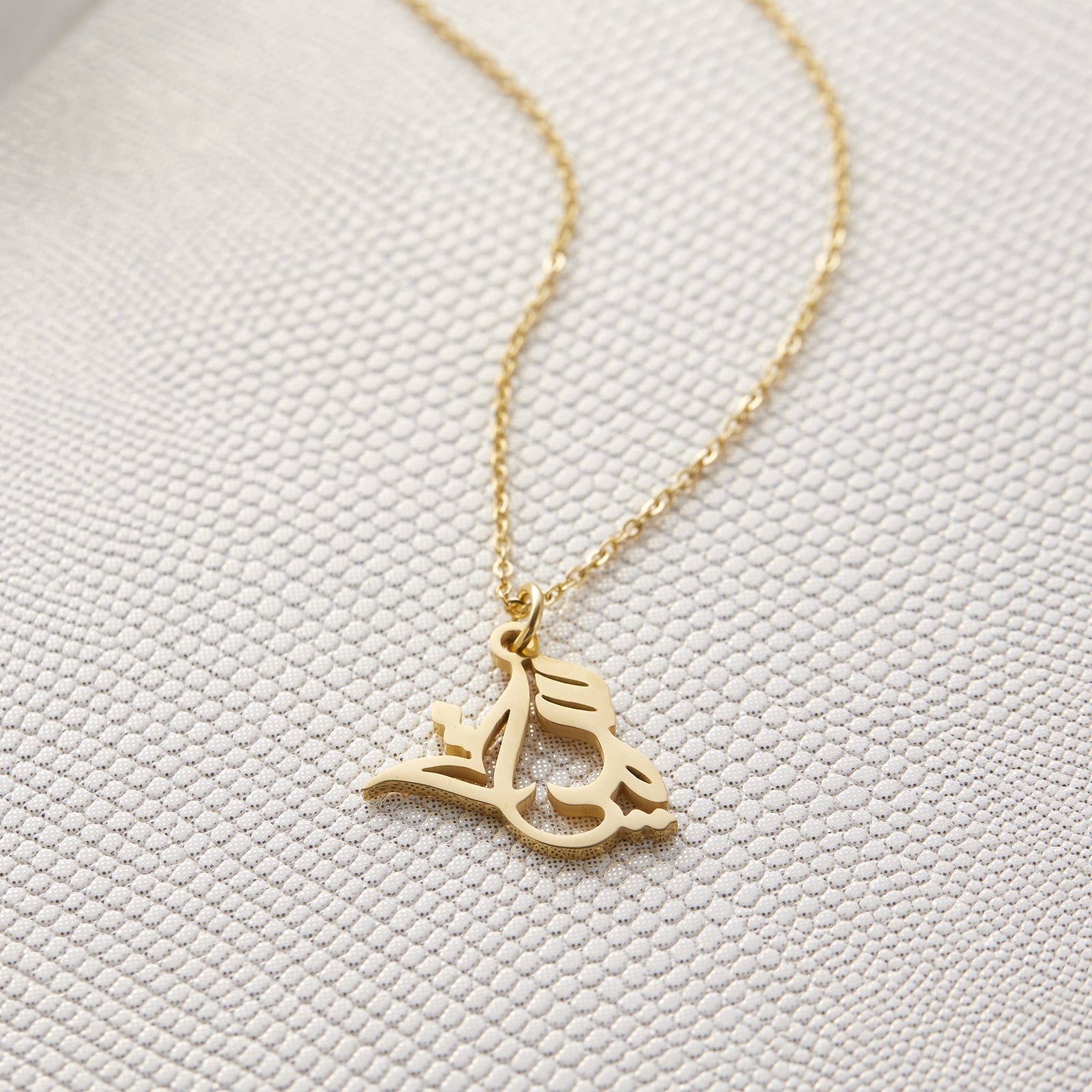 Close up of the gold Ready Calligraphy Name Necklace - Sumayya against a light background.