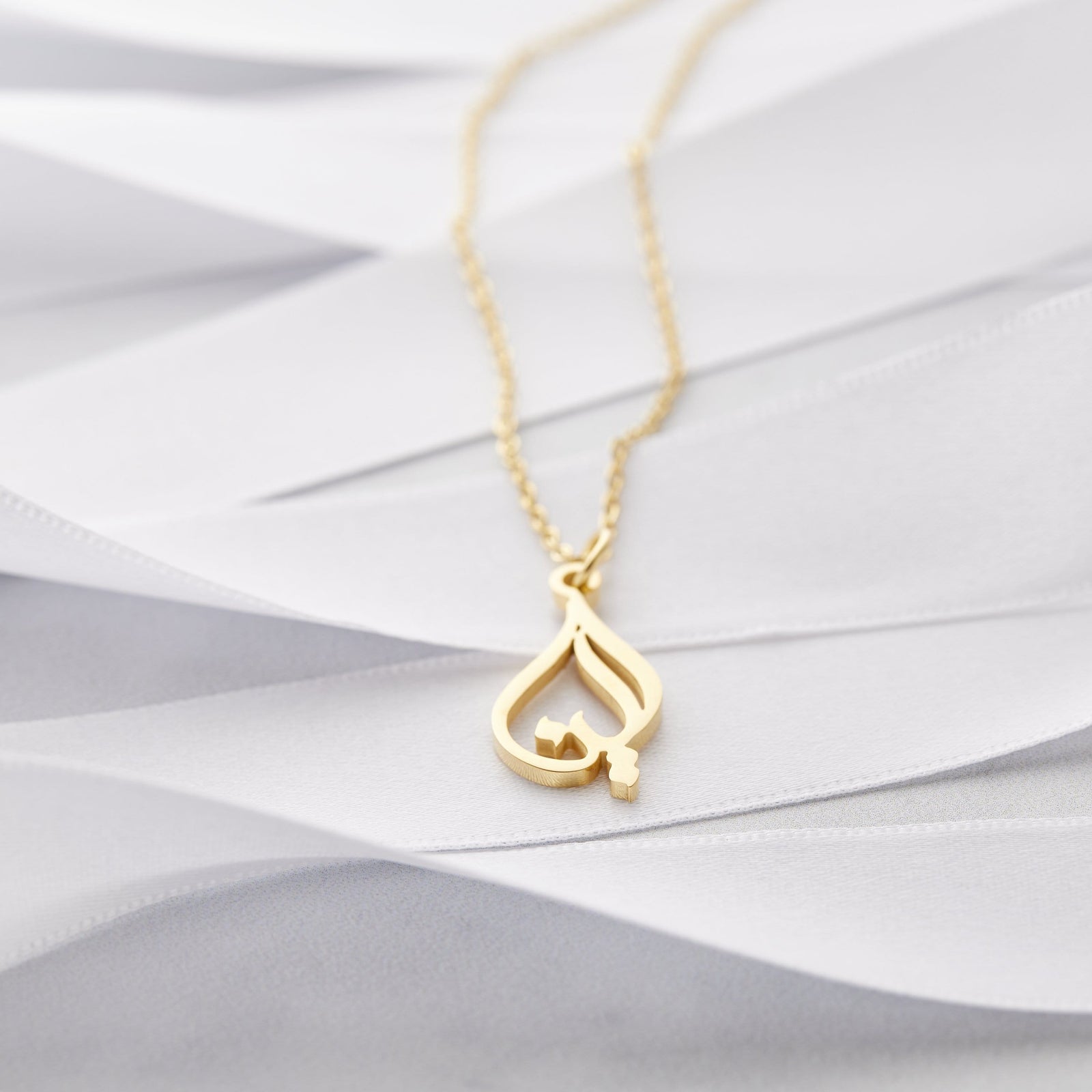 Close up of the gold Ready Calligraphy Name Necklace - Aleena against a light background.