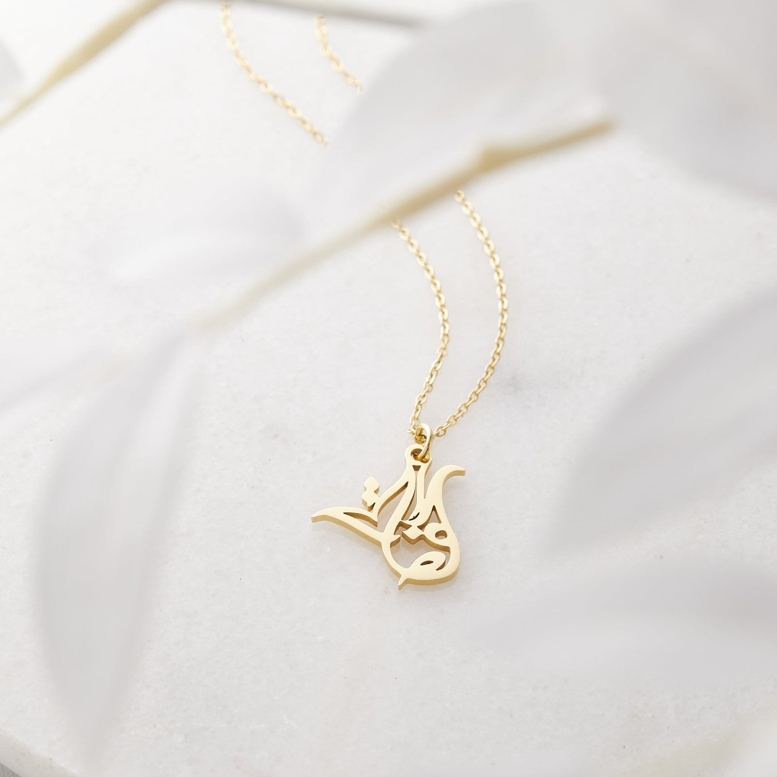Close up of the gold Ready Calligraphy Name Necklace - Hafsa against a light background.