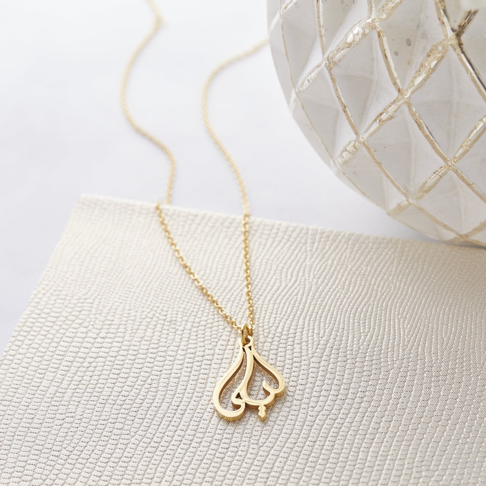 Close up of the gold Ready Calligraphy Name Necklace - Laila against a light background.