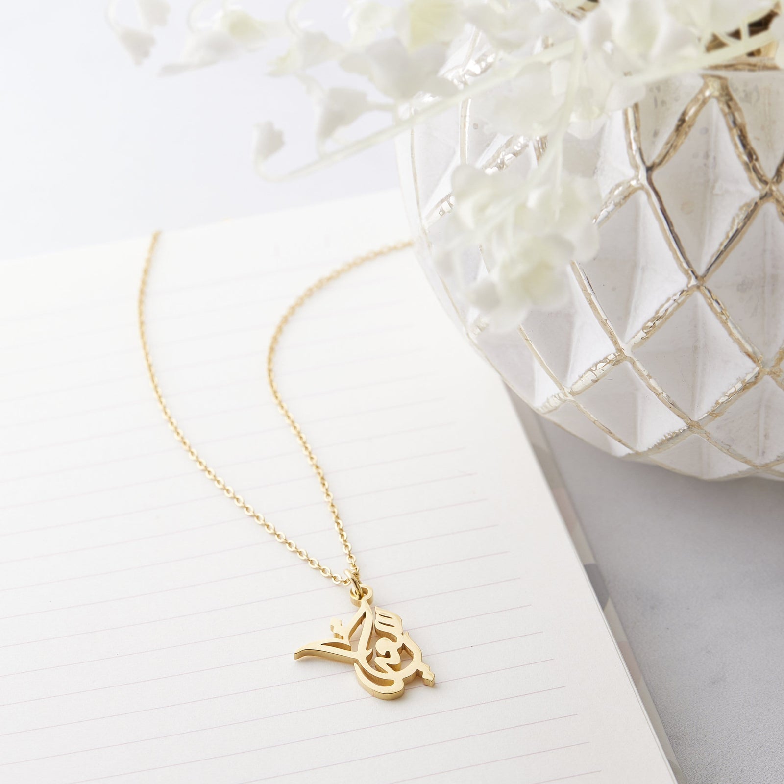 Close up of the gold Ready Calligraphy Name Necklace - Sadia against a light background.
