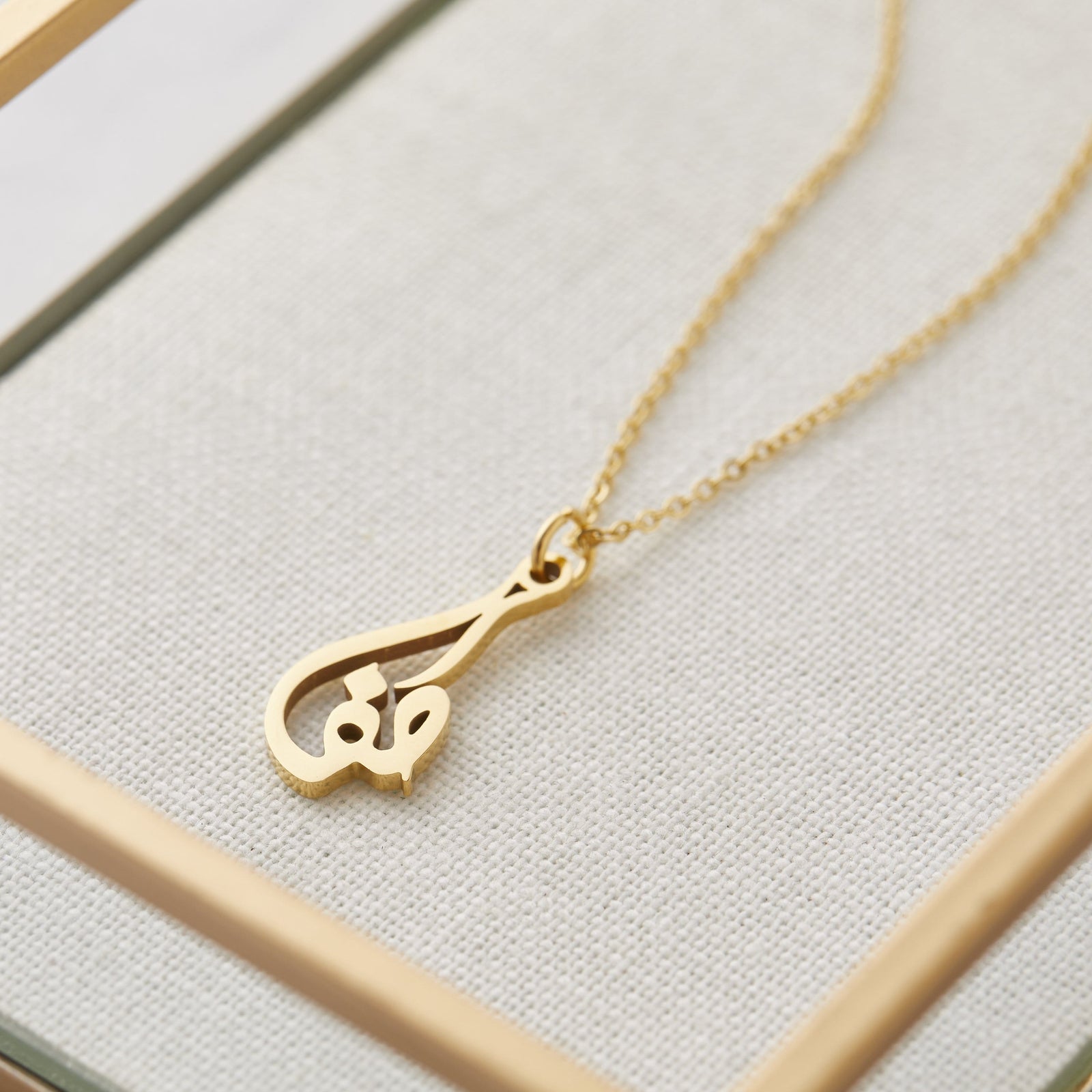 Close up of the gold Ready Calligraphy Name Necklace - Safa against a light background.
