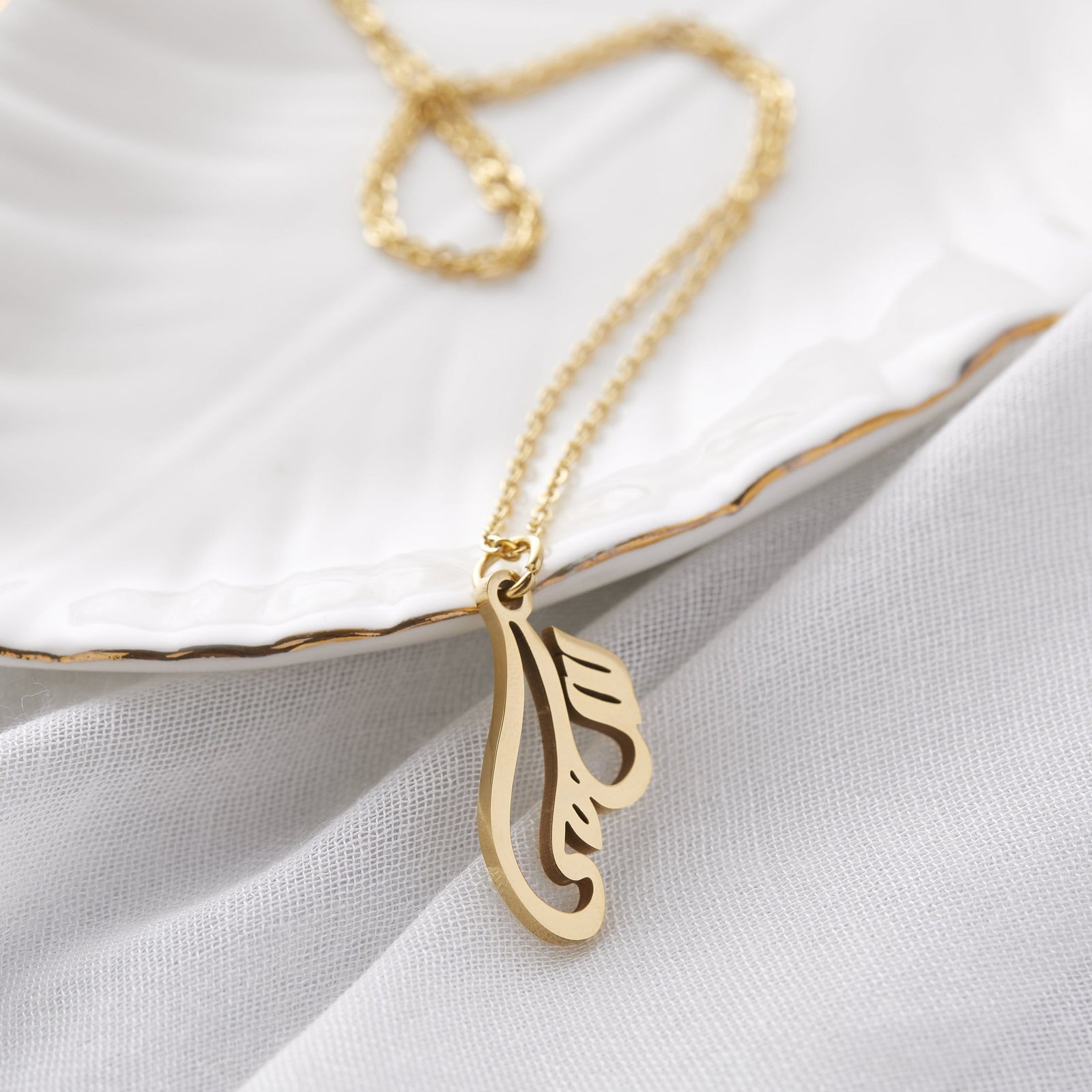 Close up of the gold Ready Calligraphy Name Necklace - Salma against a light background.