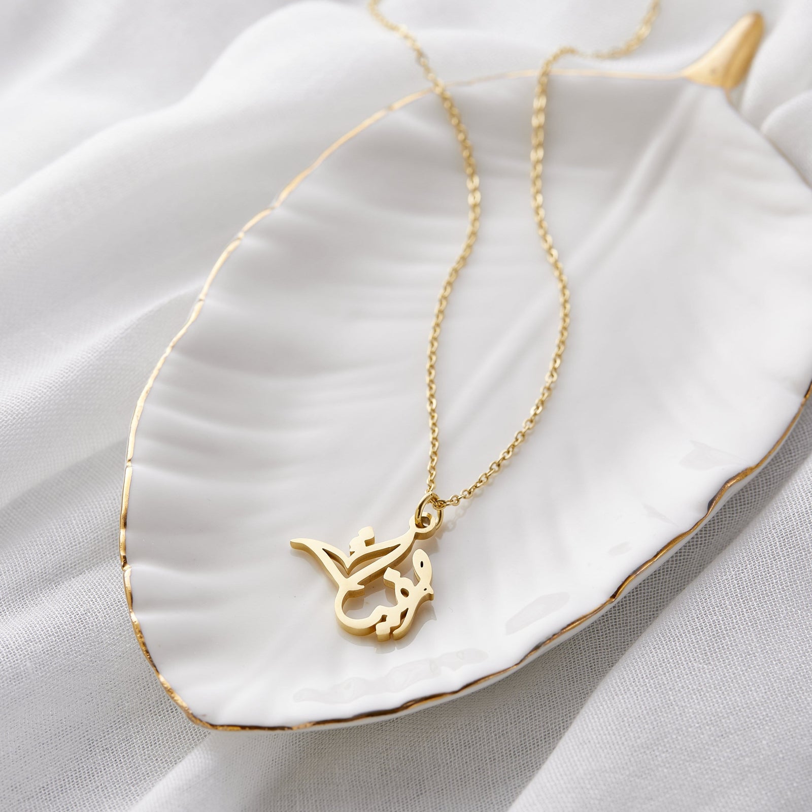 Close up of the gold Ready Calligraphy Name Necklace - Sophia against a light background.