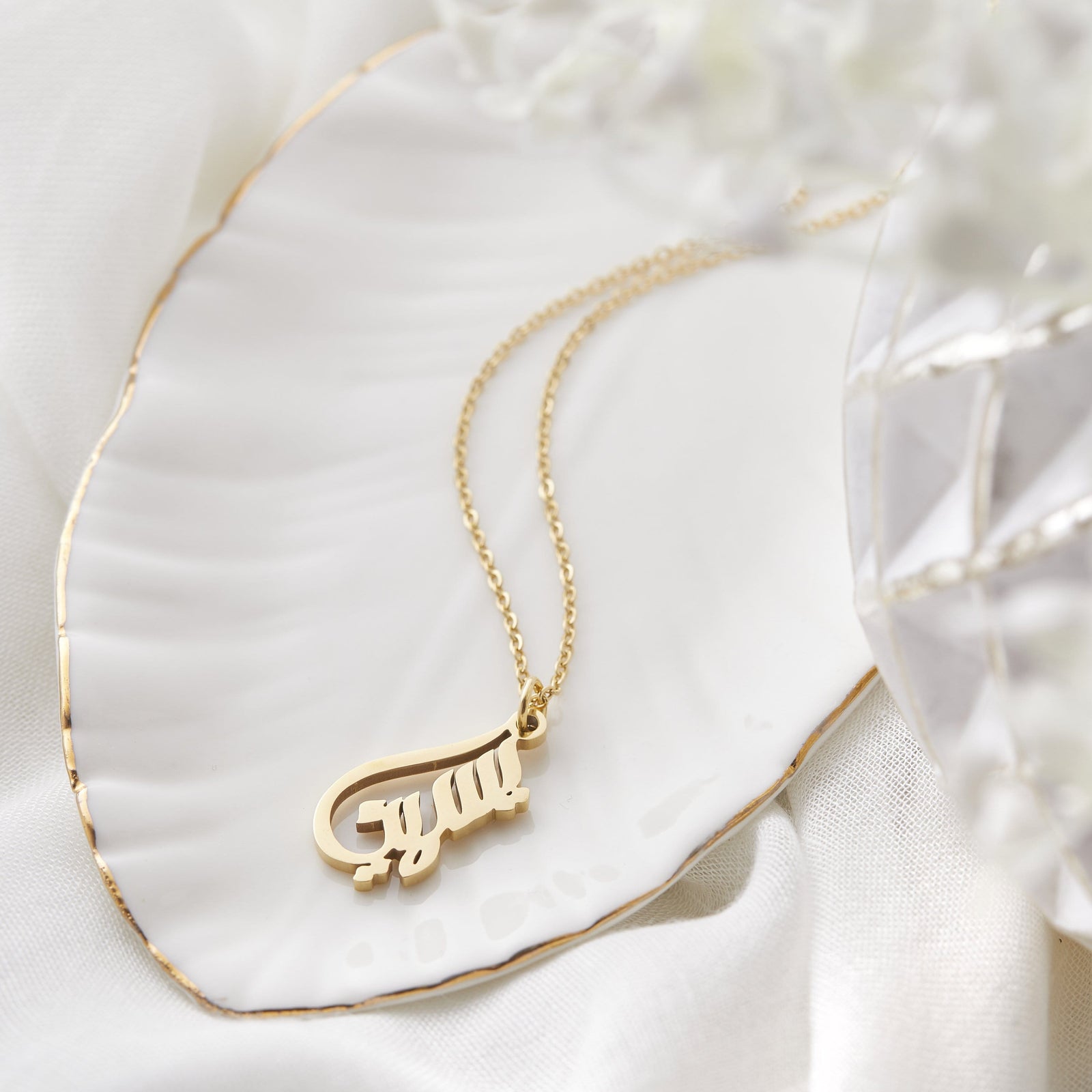 Close up of the gold Ready Calligraphy Name Necklace - Yasmine against a light background.