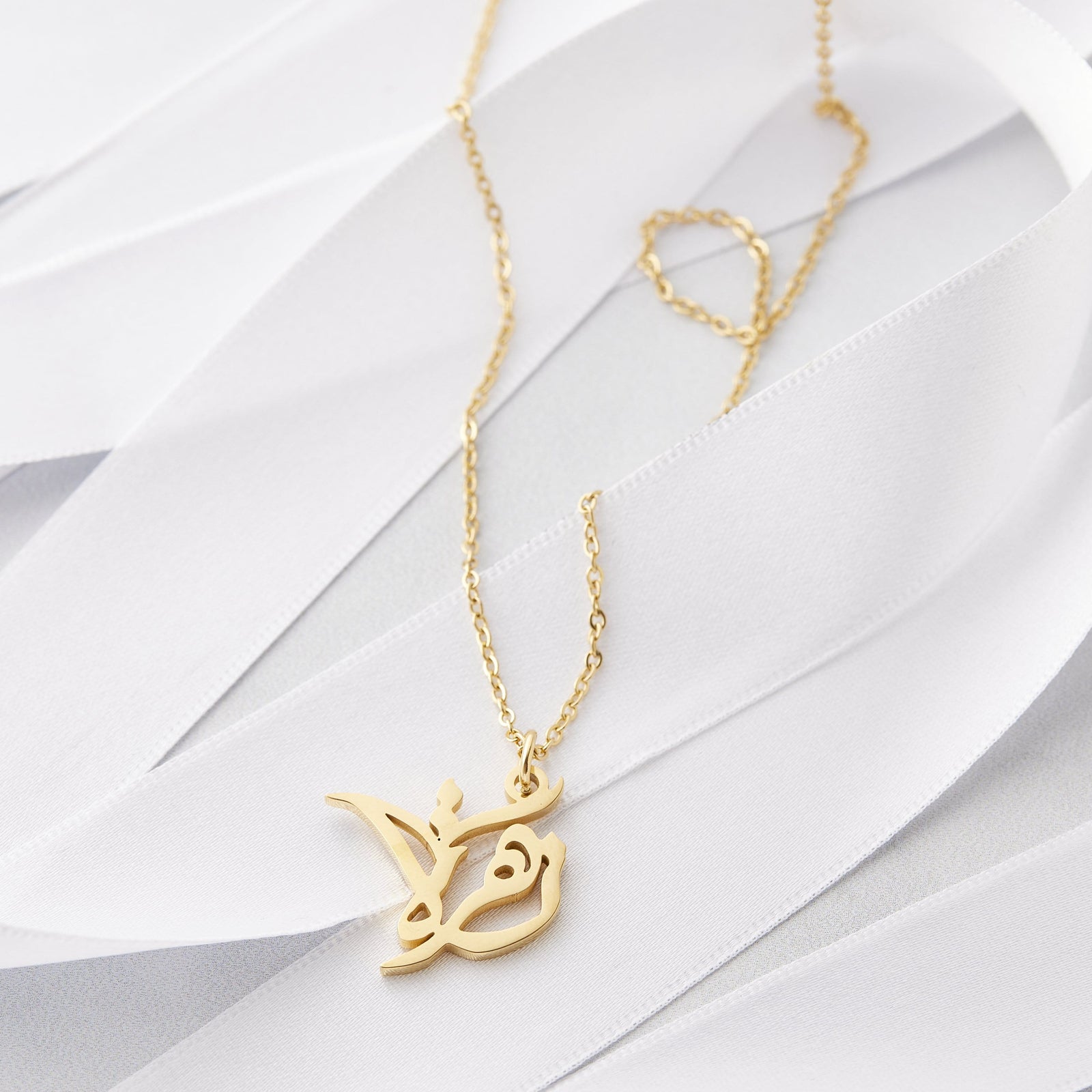 Close up of the gold Ready Calligraphy Name Necklace - Zahra against a light background.