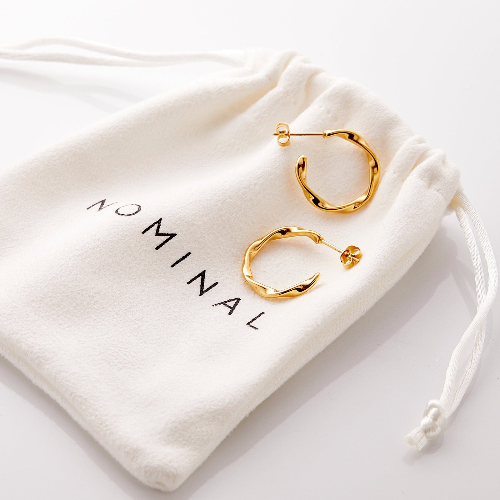 The gold Ripple Hoop Earrings resting on the Nominal pouch.