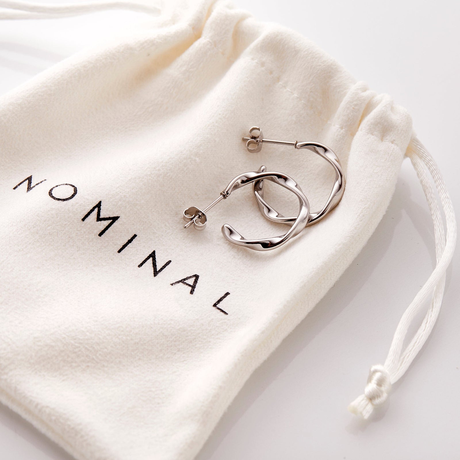The gold Ripple Hoop Earrings resting on the Nominal pouch.