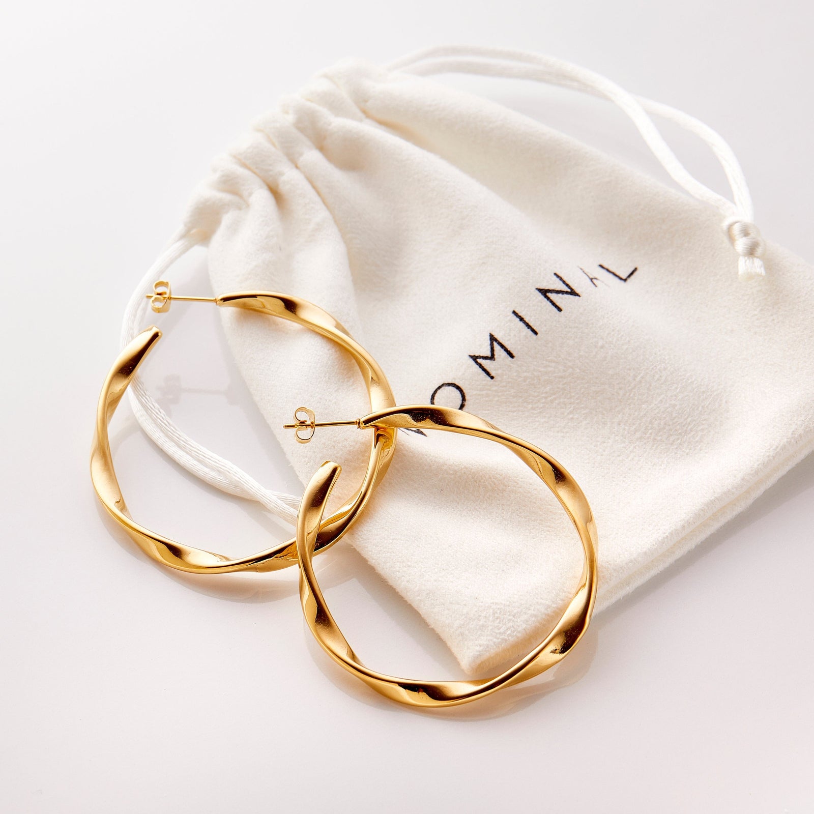 Flat lay of the Ripple Hoop Earrings resting on the Nominal Pouch