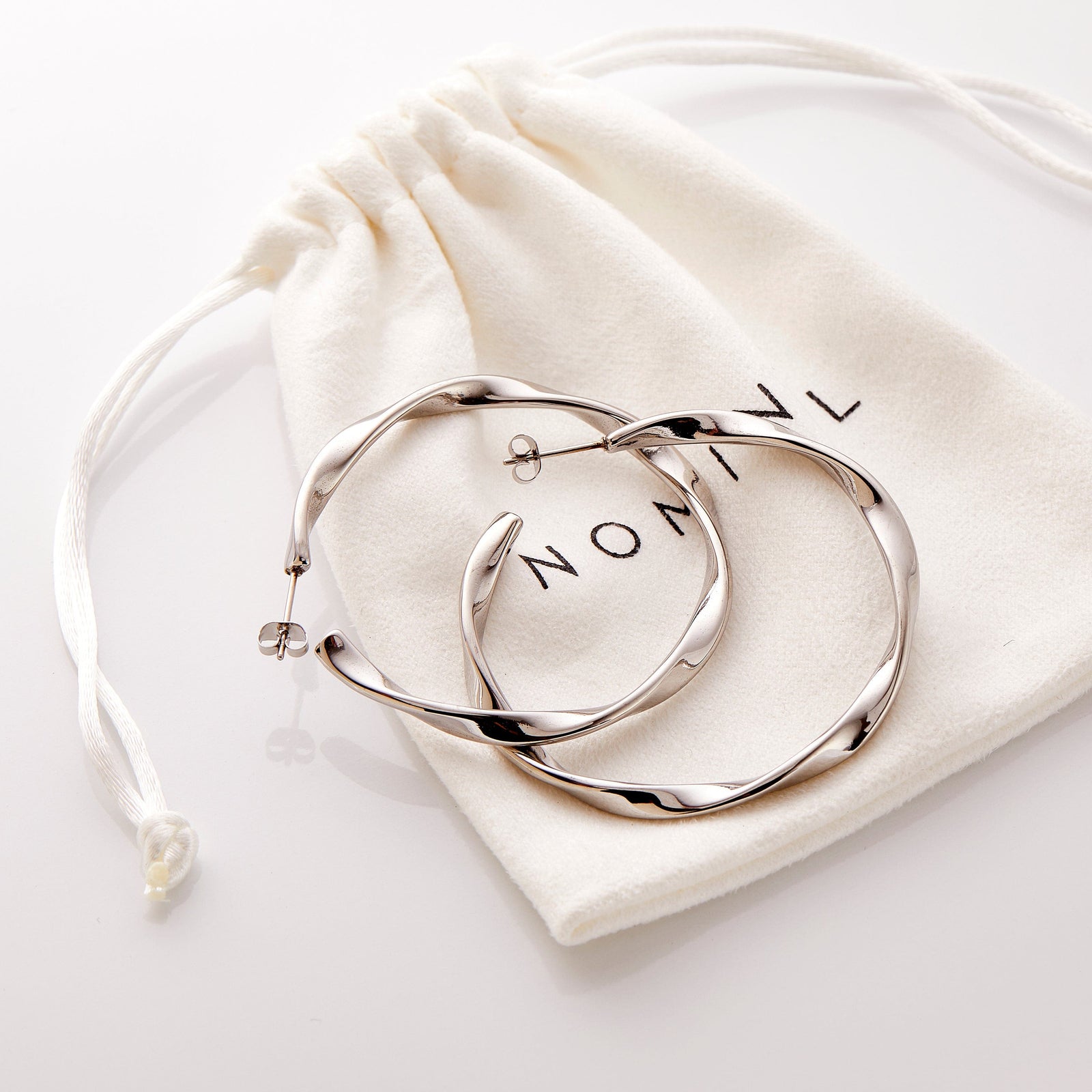 The silver Ripple Hoop Earrings resting on the Nominal pouch.