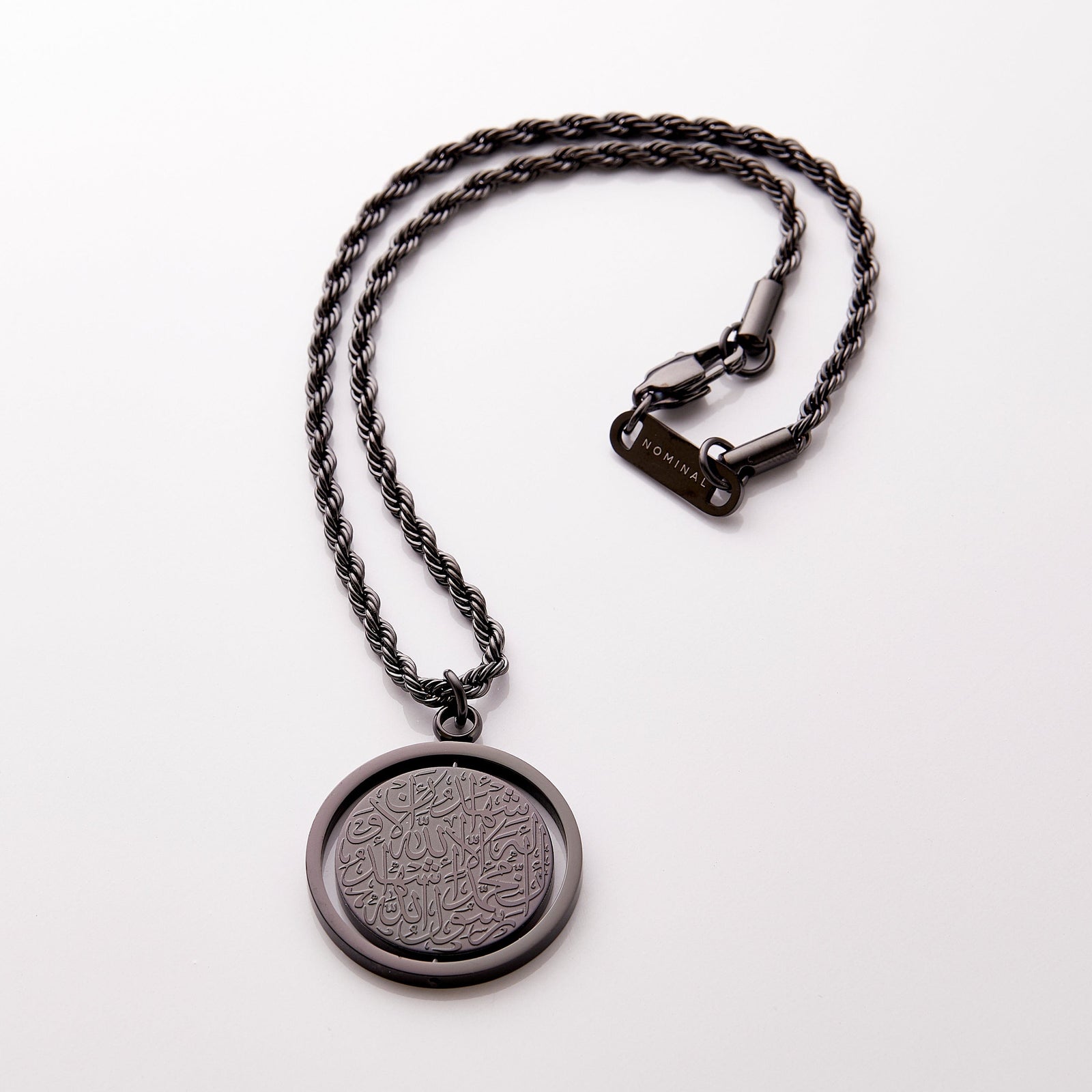 Black car hanger with a circular pendant engraved in Arabic calligraphy of the Shahada, styled flat against a neutral background.